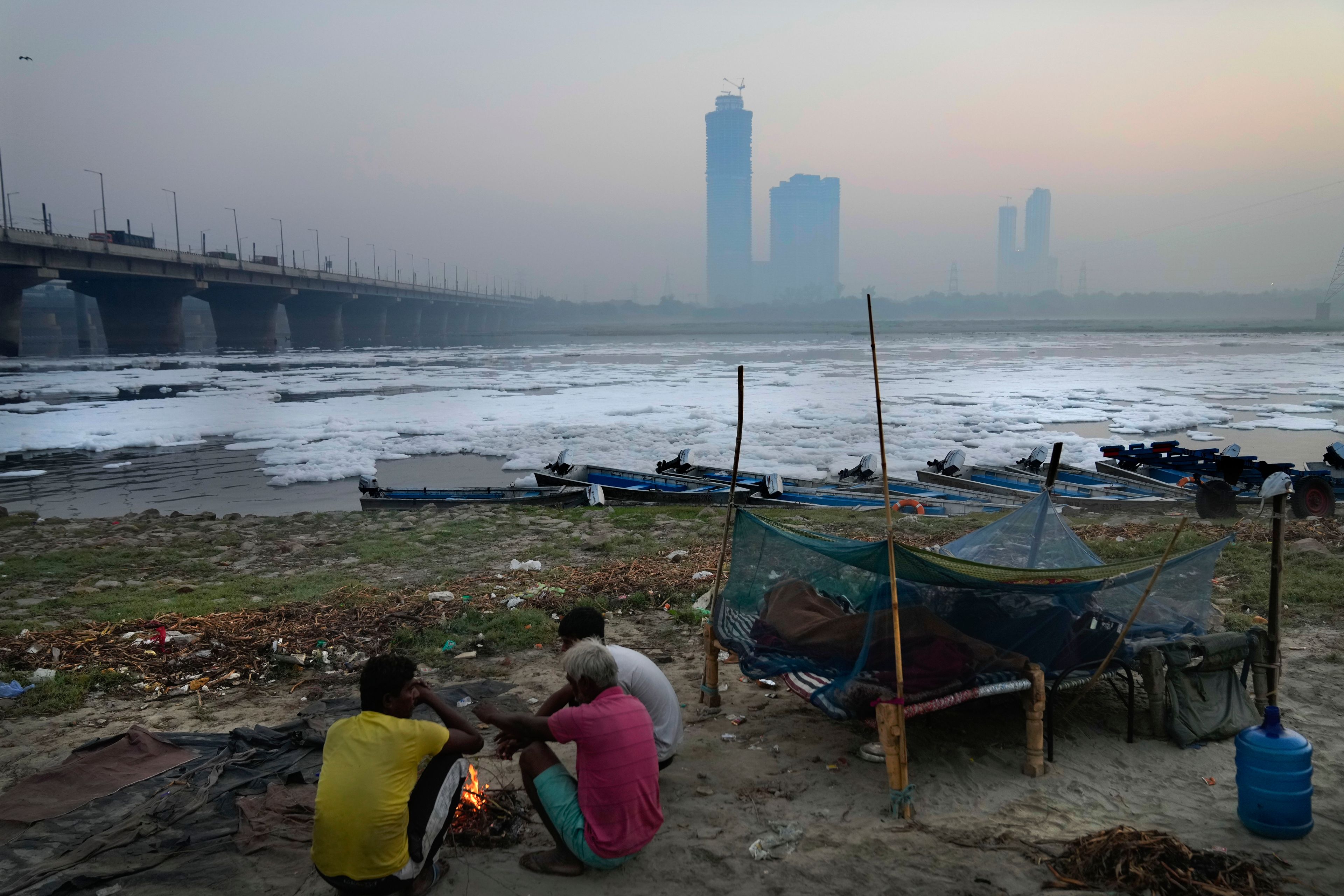 Worker warm themselves in front of a bonfire sitting on the banks of the river Yamuna as toxic foam floats, in New Delhi, India, Tuesday, Oct. 29, 2024. (AP Photo/Manish Swarup)