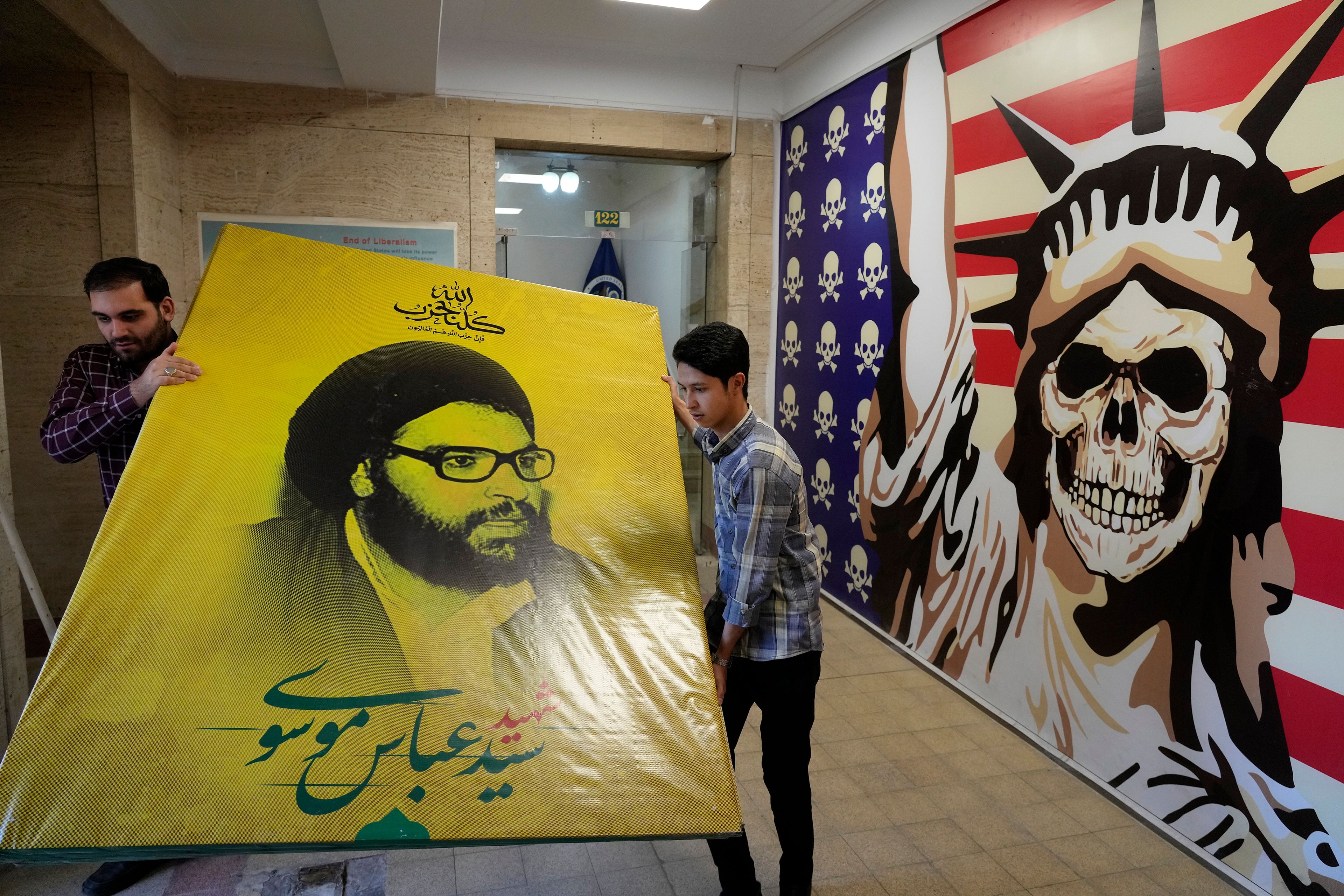 Two men carry a banner of the late Hezbollah leader Sheik Abbas al-Mousawi, who was killed by an Israeli airstrike in 1992, next to a satirised image of the Statue of Liberty and the U.S. flag at the former U.S. Embassy, which has been turned into an anti-American museum, in Tehran, Iran, Tuesday, Oct. 22, 2024. (AP Photo/Vahid Salemi)