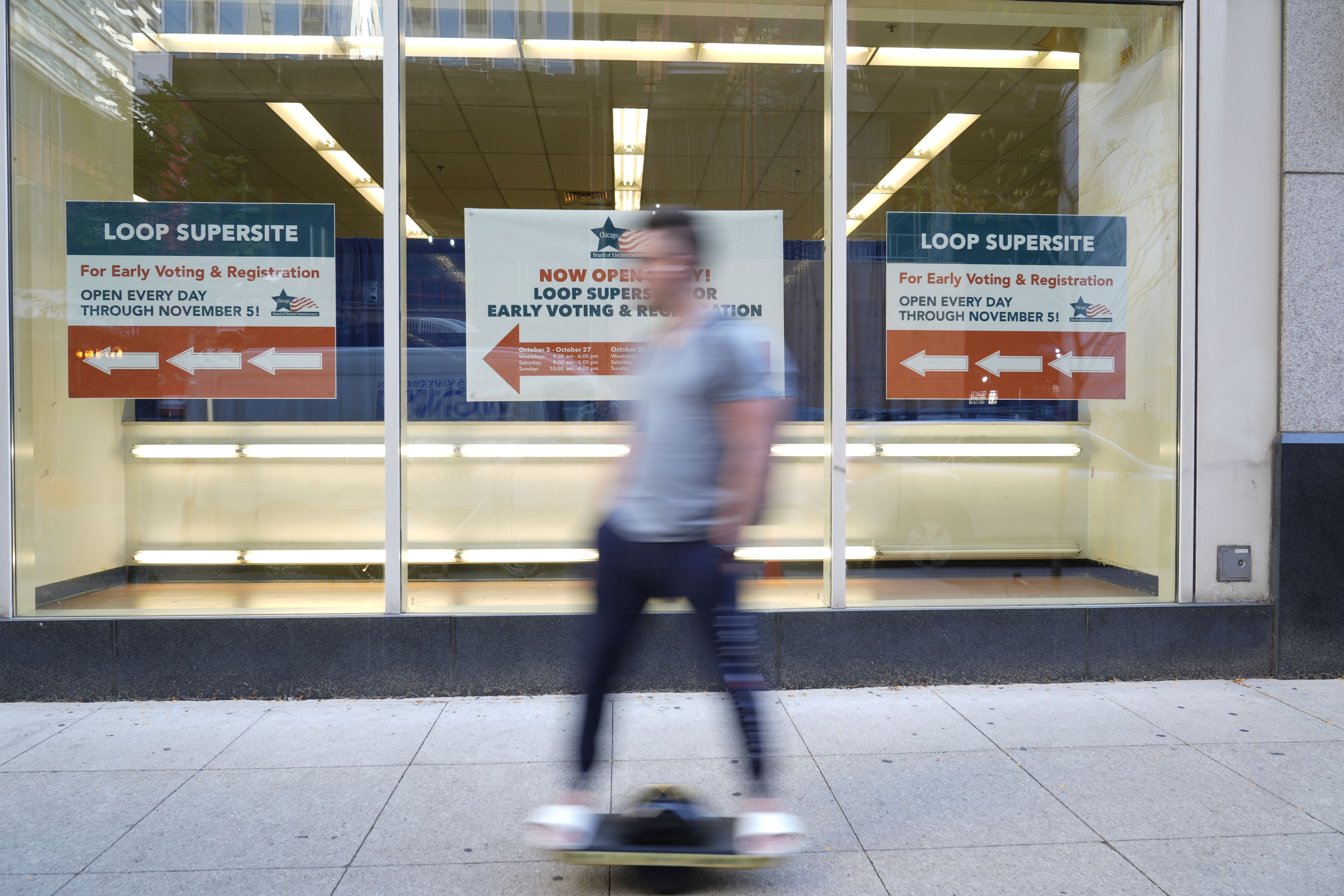 A person skateboards past a sign for early voting for the 2024 Presidential General Election, Thursday, Oct. 3, 2024 in Chicago. (AP Photo/Charles Rex Arbogast)