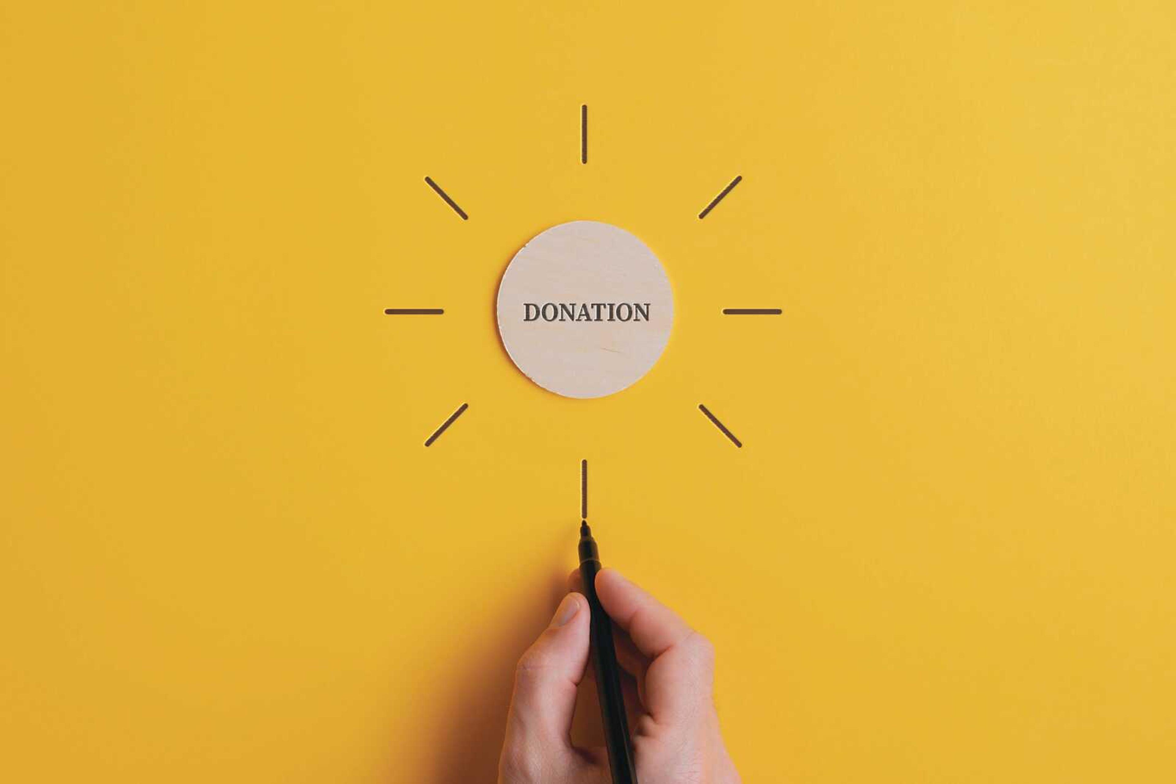 Word donation written on a wooden cut circle with male hand drawing rays around it in a conceptual image.