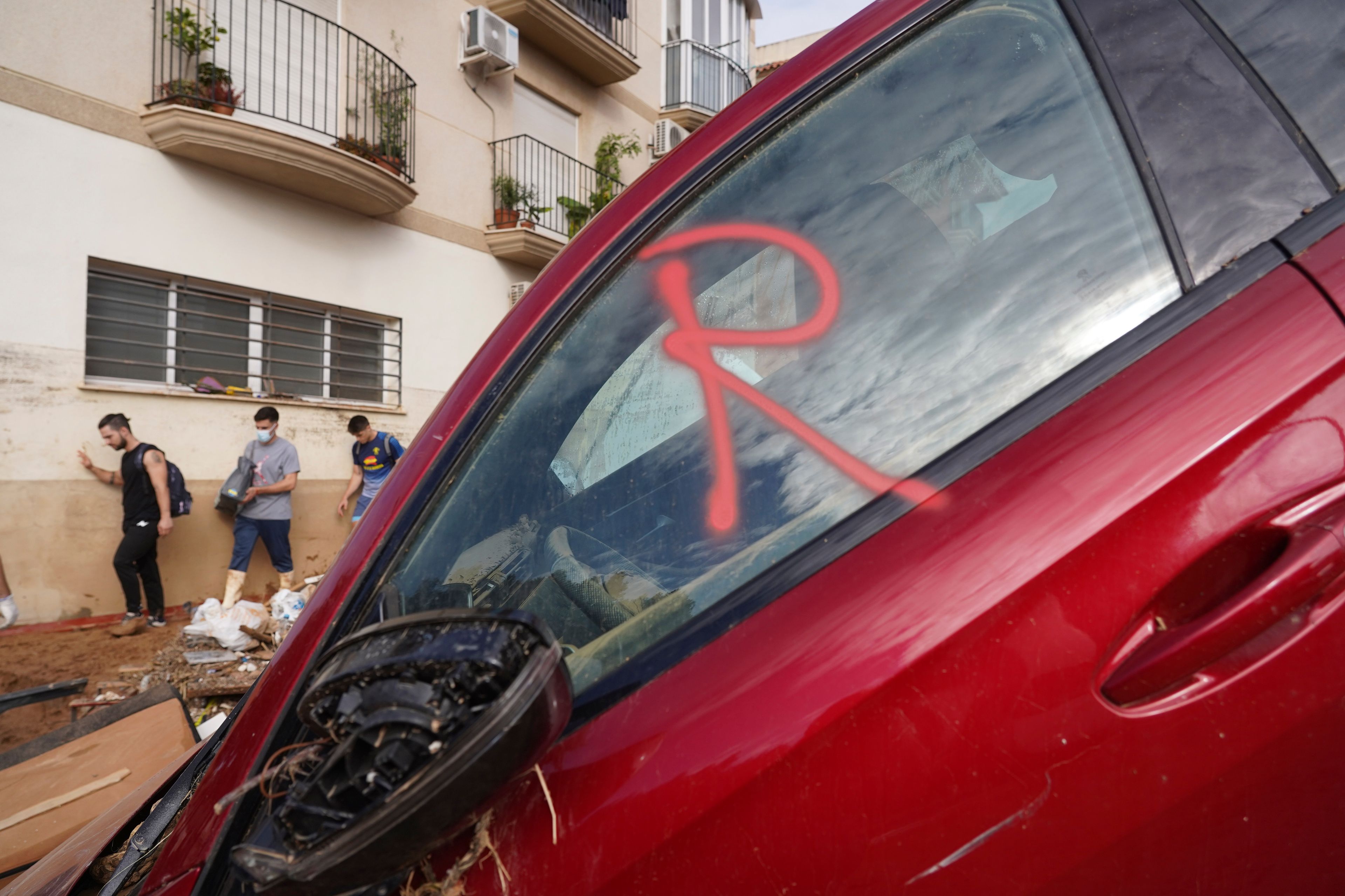 Volunteers helping with the clean up operation walk by a car with the letter R painted on the window meaning it has been revised as rescue workers look for bodies after floods in Massanassa, just outside of Valencia, Spain, Saturday, Nov. 2, 2024. (AP Photo/Alberto Saiz)