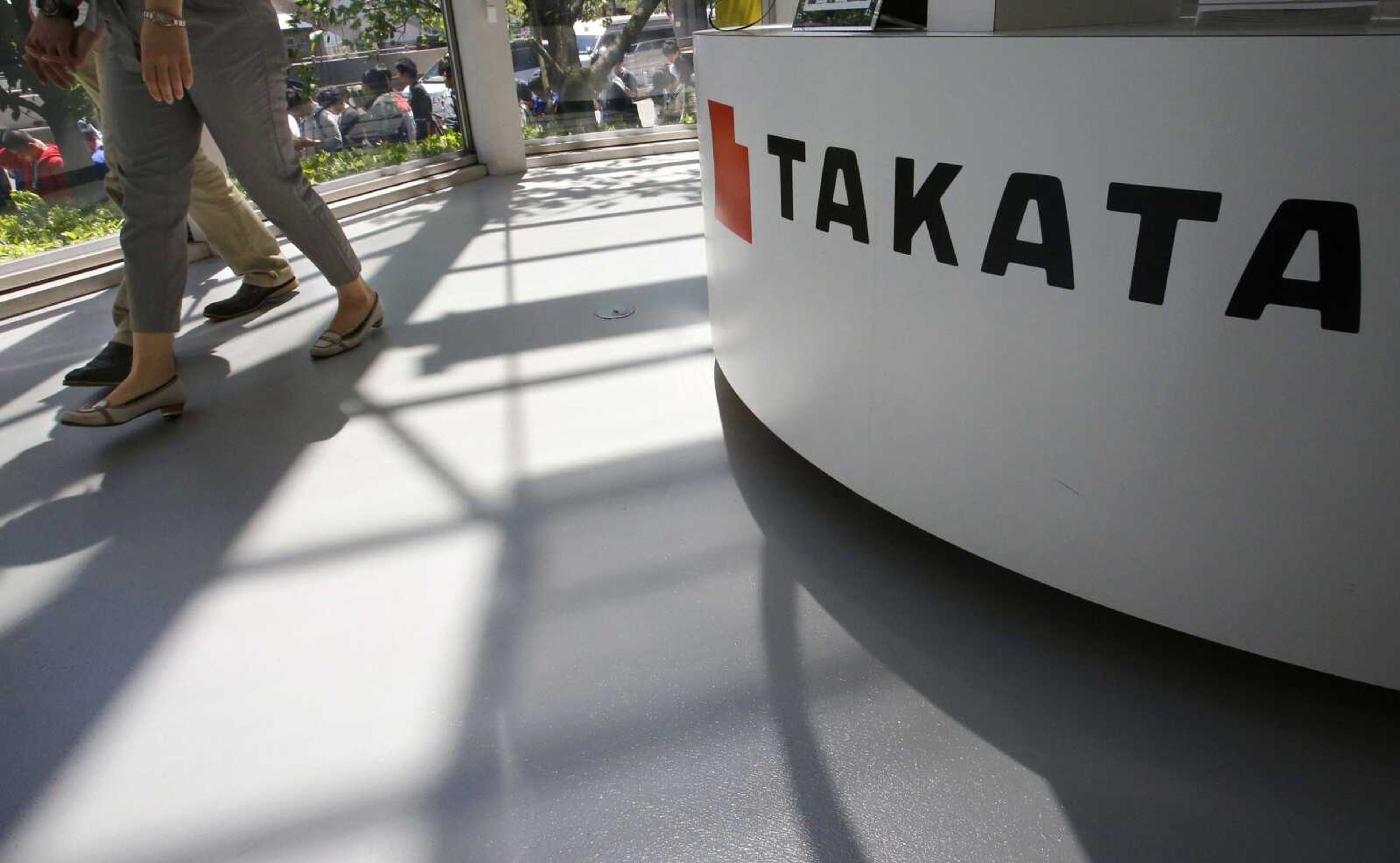 Visitors walk by a Takata Corp. desk at an automaker's showroom in Tokyo.