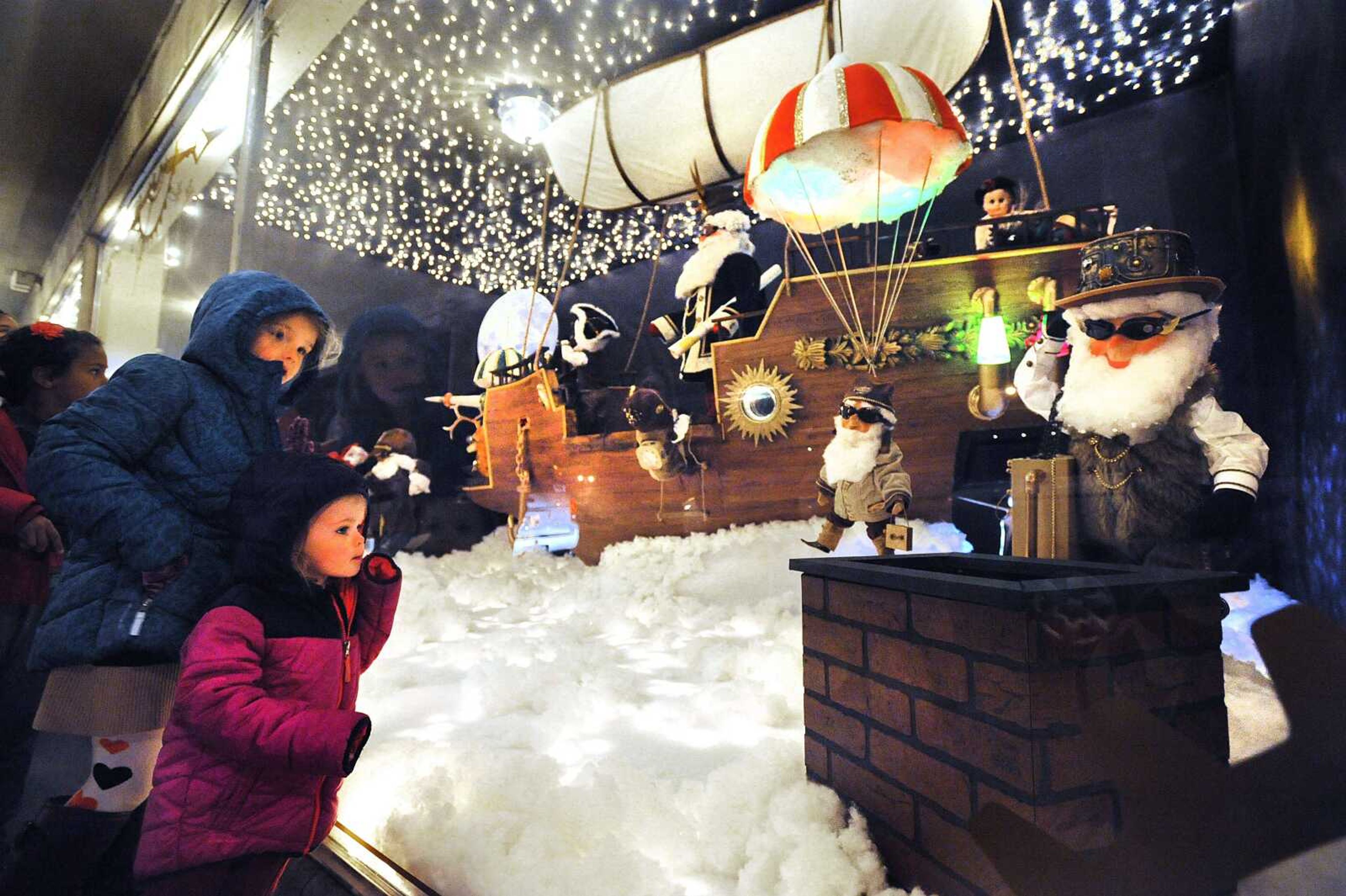 Ainsley Cook, 2, and her big sister Adeline, 6, check out Santa and his helpers in the window of Hutson's FIne Furniture, Thursday, Nov. 27, 2014, in downtown Cape Girardeau. This year's brand new Christmas display is based on a Victorian airship. Many families have a tradition of stopping at Hutson's window after their Thanksgiving meals, and follow the display with a trip to Cape County Park North for the Holiday of Lights display. (Laura Simon)