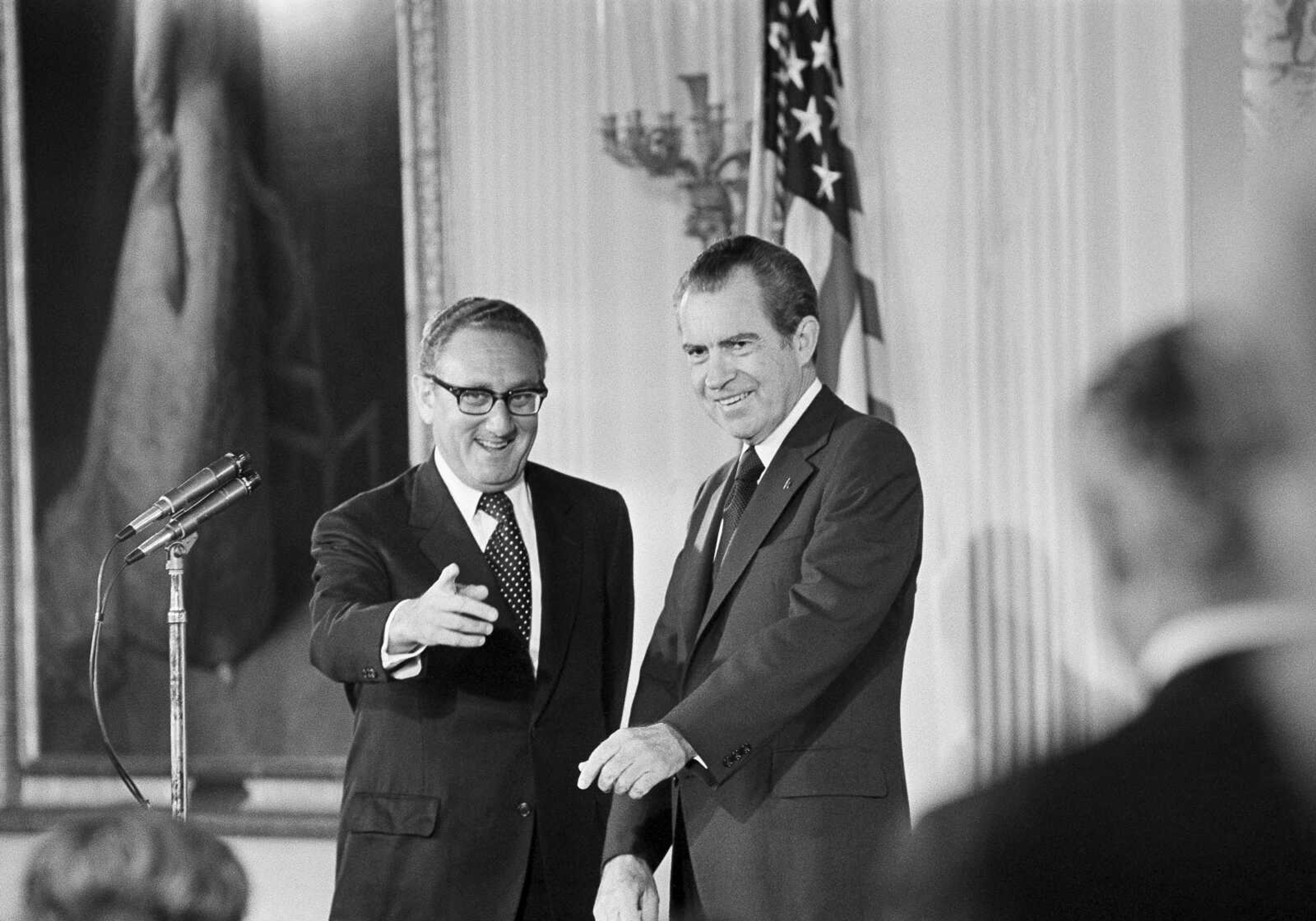 Secretary of State Henry Kissinger, left, gestures to the audience in the East Room of the White House on Sept. 22, 1973, as President Richard Nixon watches, in Washington. Kissinger had just been sworn in as the 56th secretary of state.