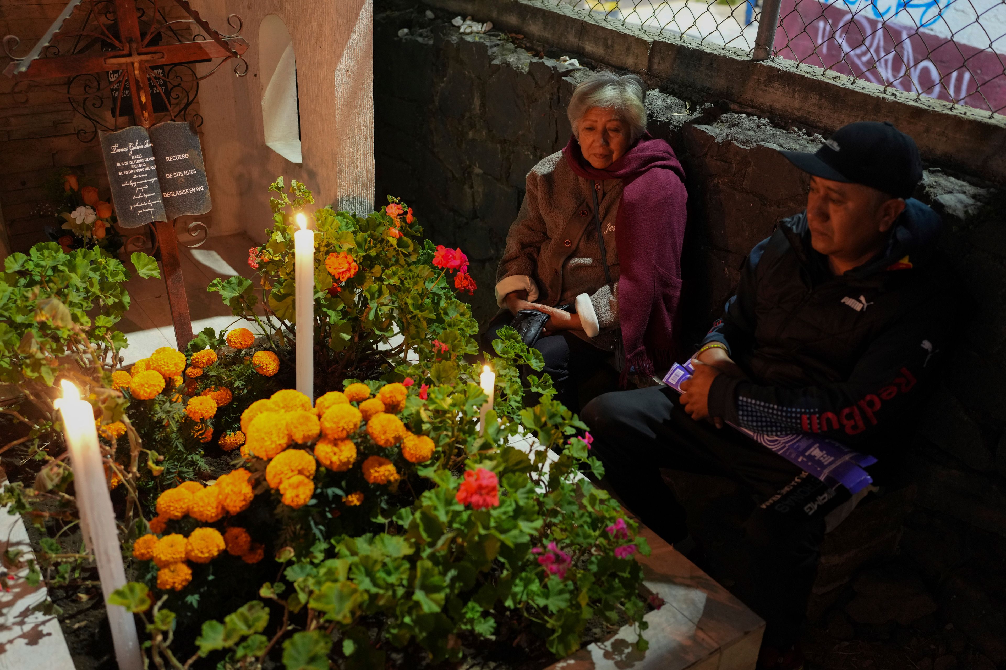 Juana Godoy, left, and Isaac Gonzalez sit at the tomb of their dearly departed, as they celebrate the Day of the Dead, at the San Gregorio Atlapulco cemetery on the outskirts of Mexico City, Friday, Nov. 1, 2024. (AP Photo/Moises Castillo)