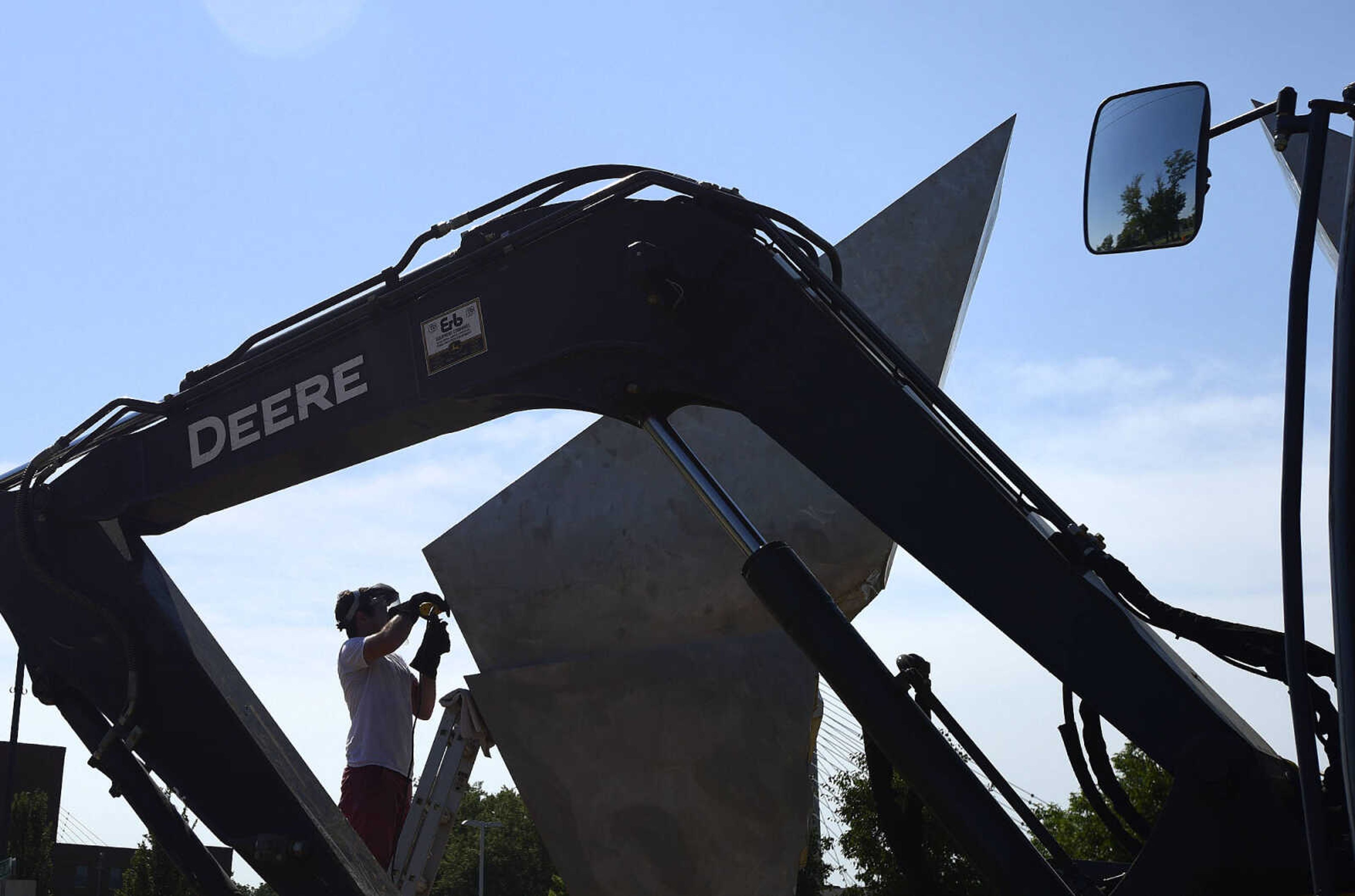 Terry Davis polishes a portion of Chris Wubbena's sculpture, "Commence" after its installation in the Fountain Street roundabout on Monday, July 24, 2017, near the River Campus in Cape Girardeau.