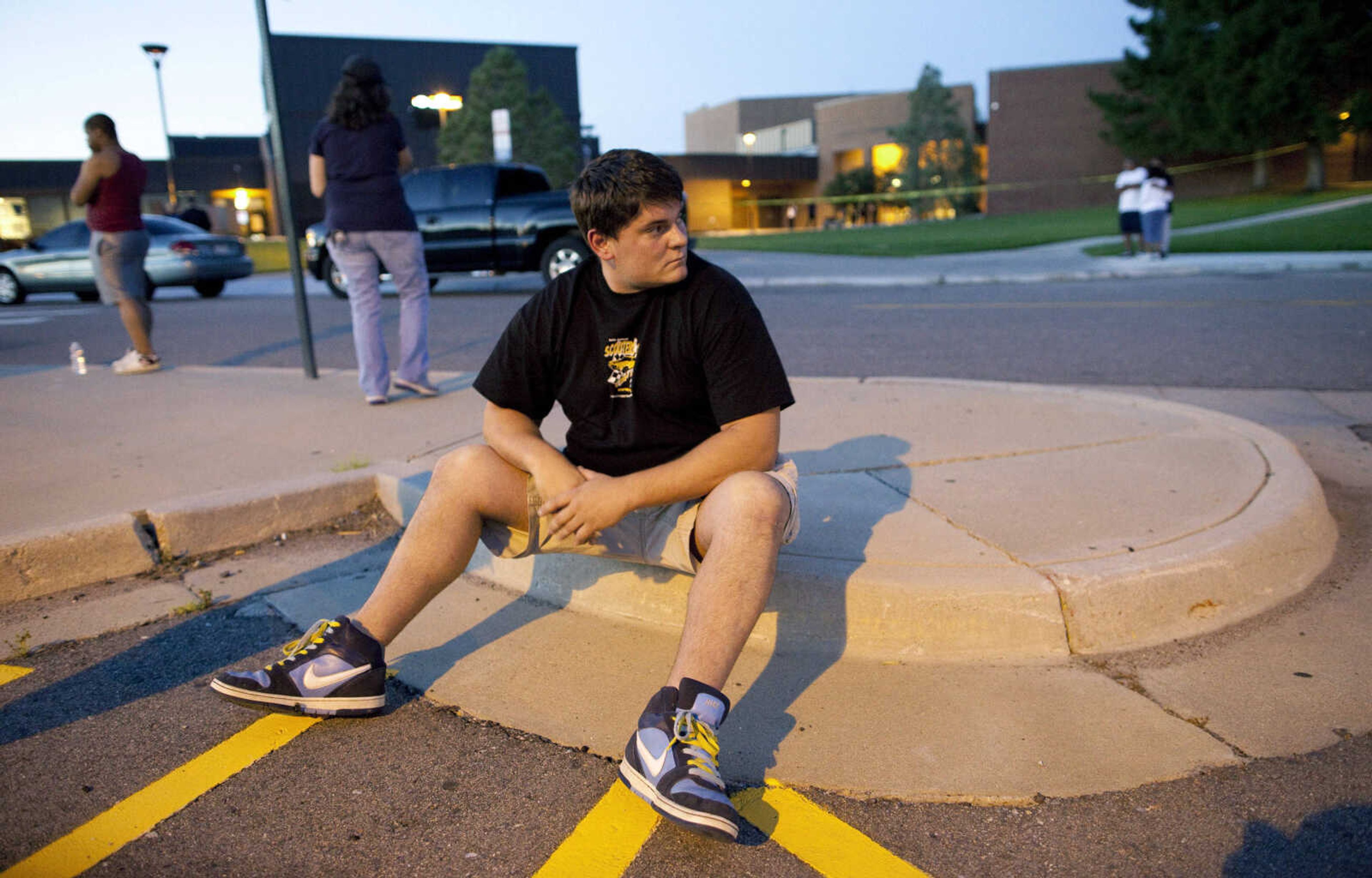 Eyewitness Chandler Brannon, 25, sits outside Gateway High School where witnesses were brought for questioning after a shooting at a movie theater showing the Batman movie "The Dark Knight Rises," Friday, July 20, 2012 in Aurora.  A gunman wearing a gas mask set off an unknown gas and fired into the crowded movie theater killing 12 people and injuring at least 50 others, authorities said. (AP Photo/Barry Gutierrez)