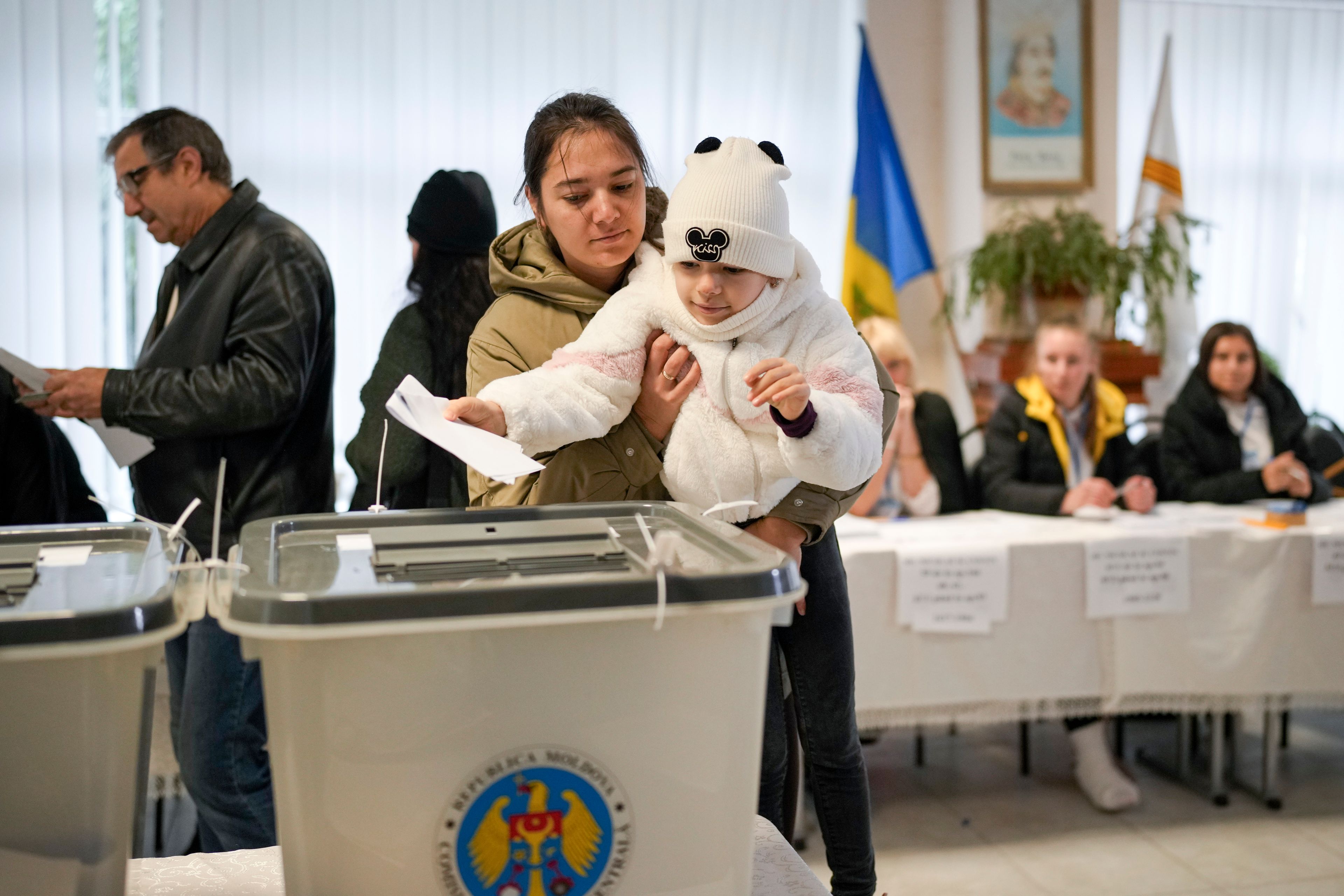 A woman holds a child as she casts her vote in Chisinau, Moldova, Sunday, Oct. 20, 2024, during a presidential election and a referendum on whether to enshrine in the Constitution the country's path to European Union membership. (AP Photo/Vadim Ghirda)