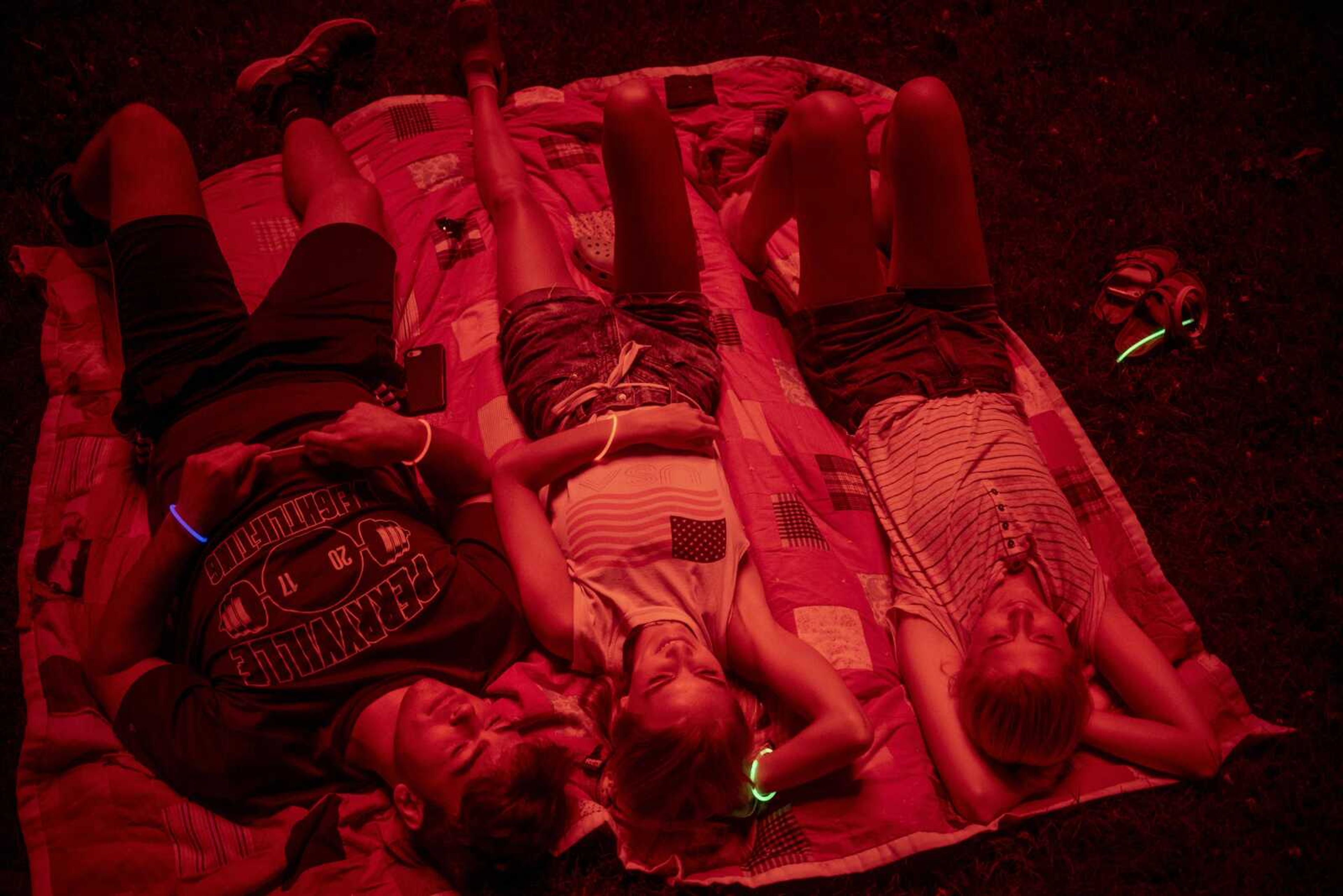 From left, Evan Daugherty, Alice Mansell and Reagan Peters are cast in red light from an exploding firework while watching an Independence Day celebration at the Jackson Municipal Band Shell.