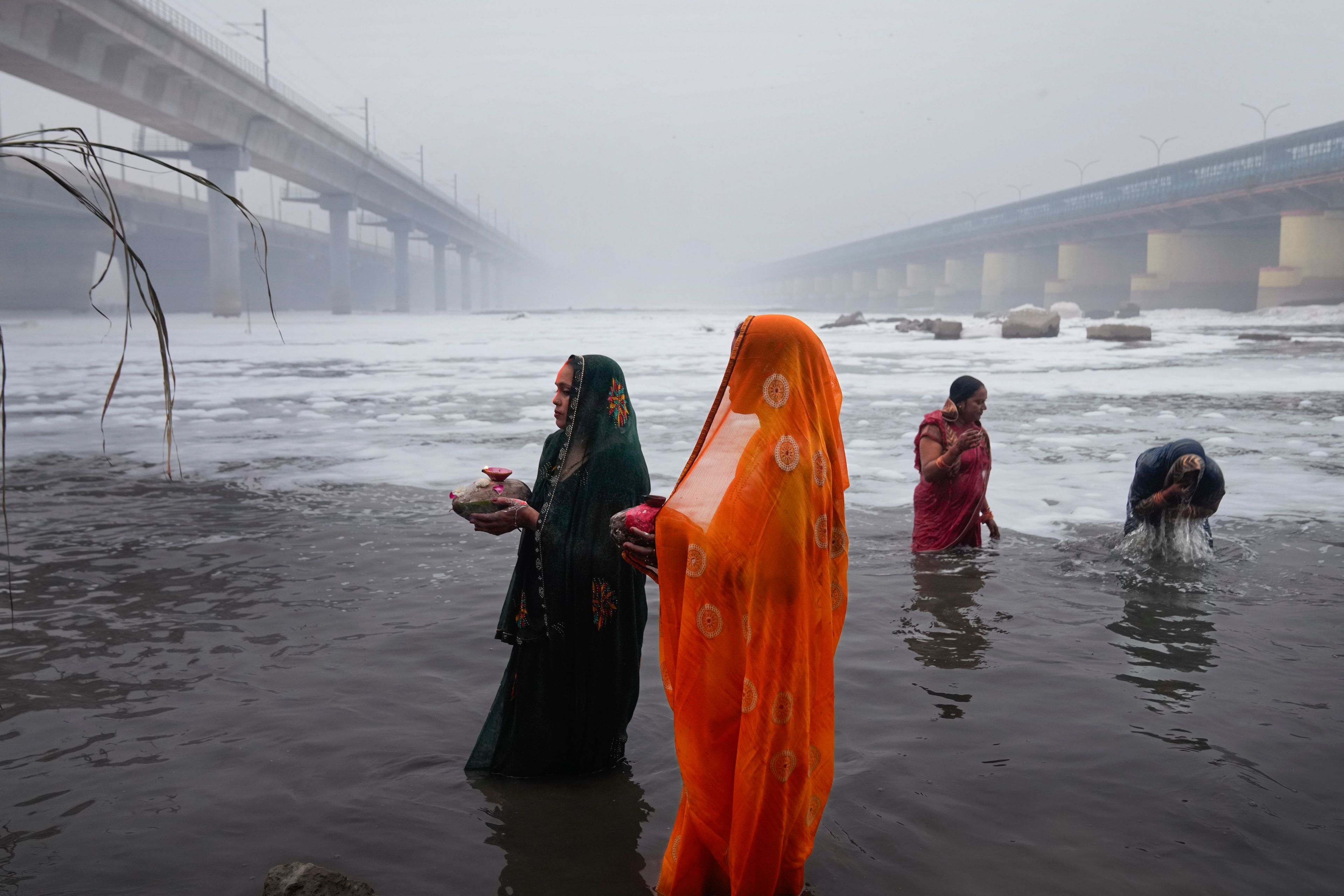 Devotees pray on the banks of the river Yamuna as toxic foam flows during Chhath festival in Noida, near New Delhi, India, Friday, Nov. 8, 2024. (AP Photo/Manish Swarup)