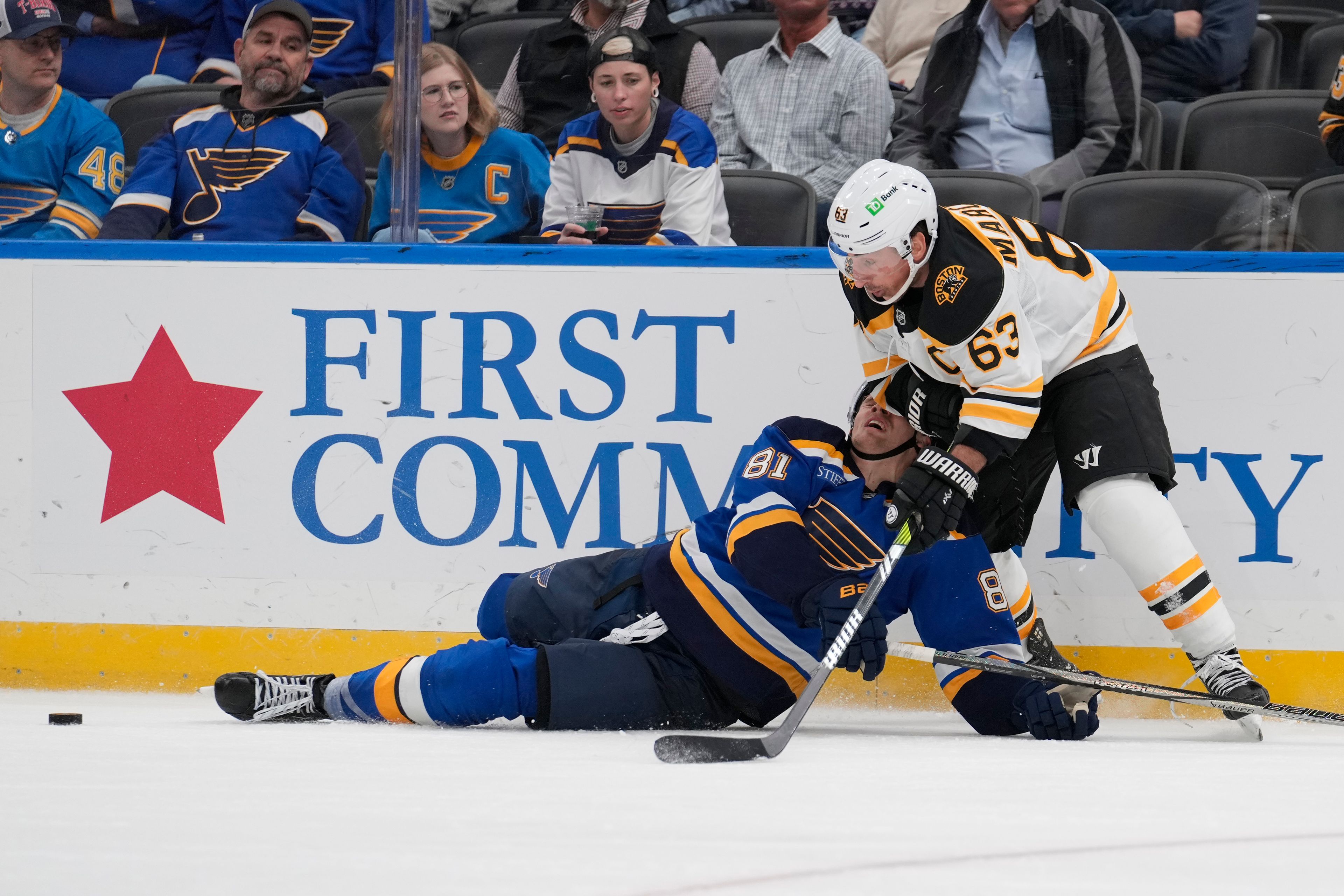 St. Louis Blues' Dylan Holloway (81) falls while battling for a loose puck with Boston Bruins' Brad Marchand (63) during the third period of an NHL hockey game Tuesday, Nov. 12, 2024, in St. Louis. (AP Photo/Jeff Roberson)