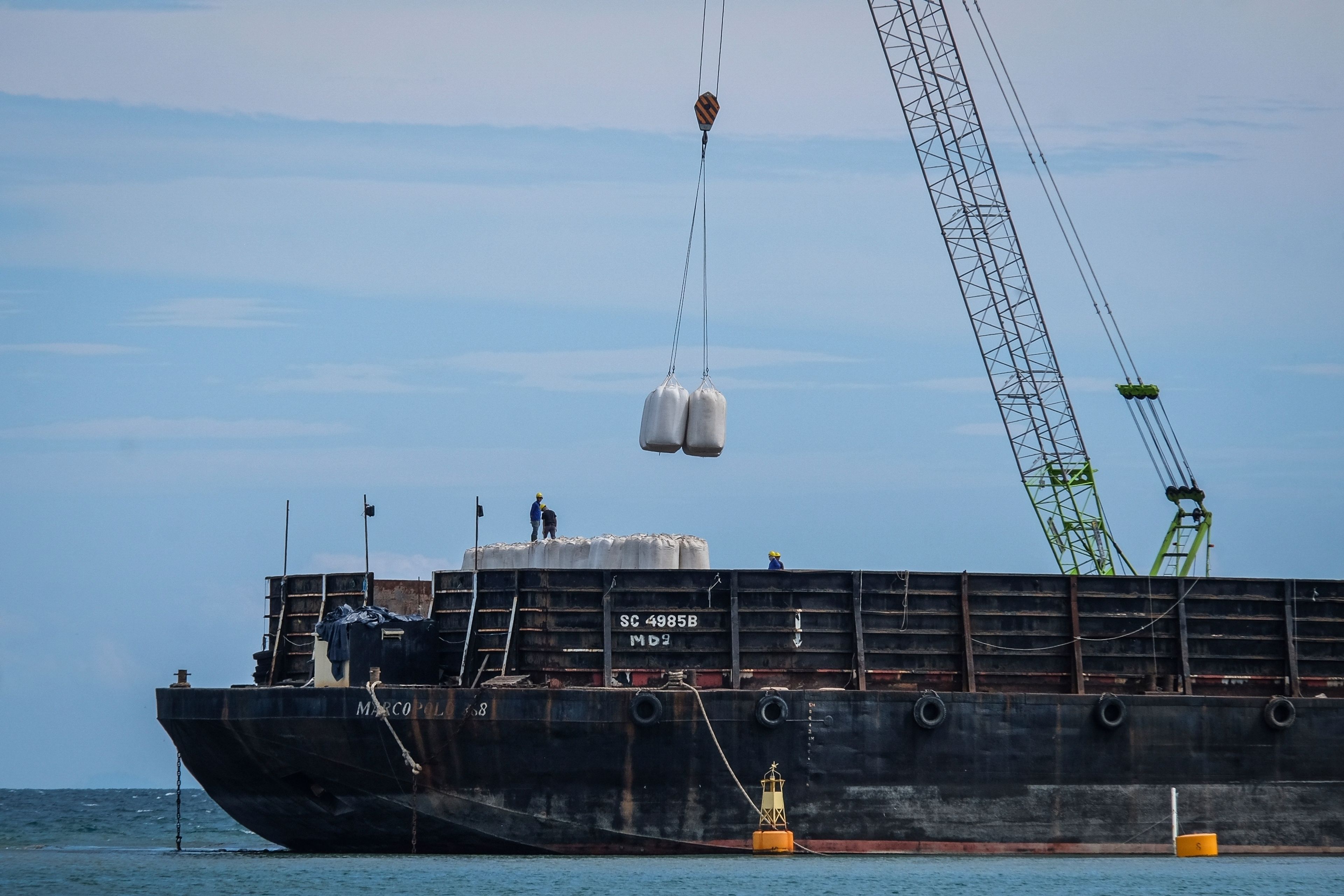 Workers load sacks of wood pellets onto a barge at a port in Pohuwato, Gorontalo province, Indonesia, Tuesday, Oct. 22, 2024. (AP Photo/Yegar Sahaduta Mangiri)