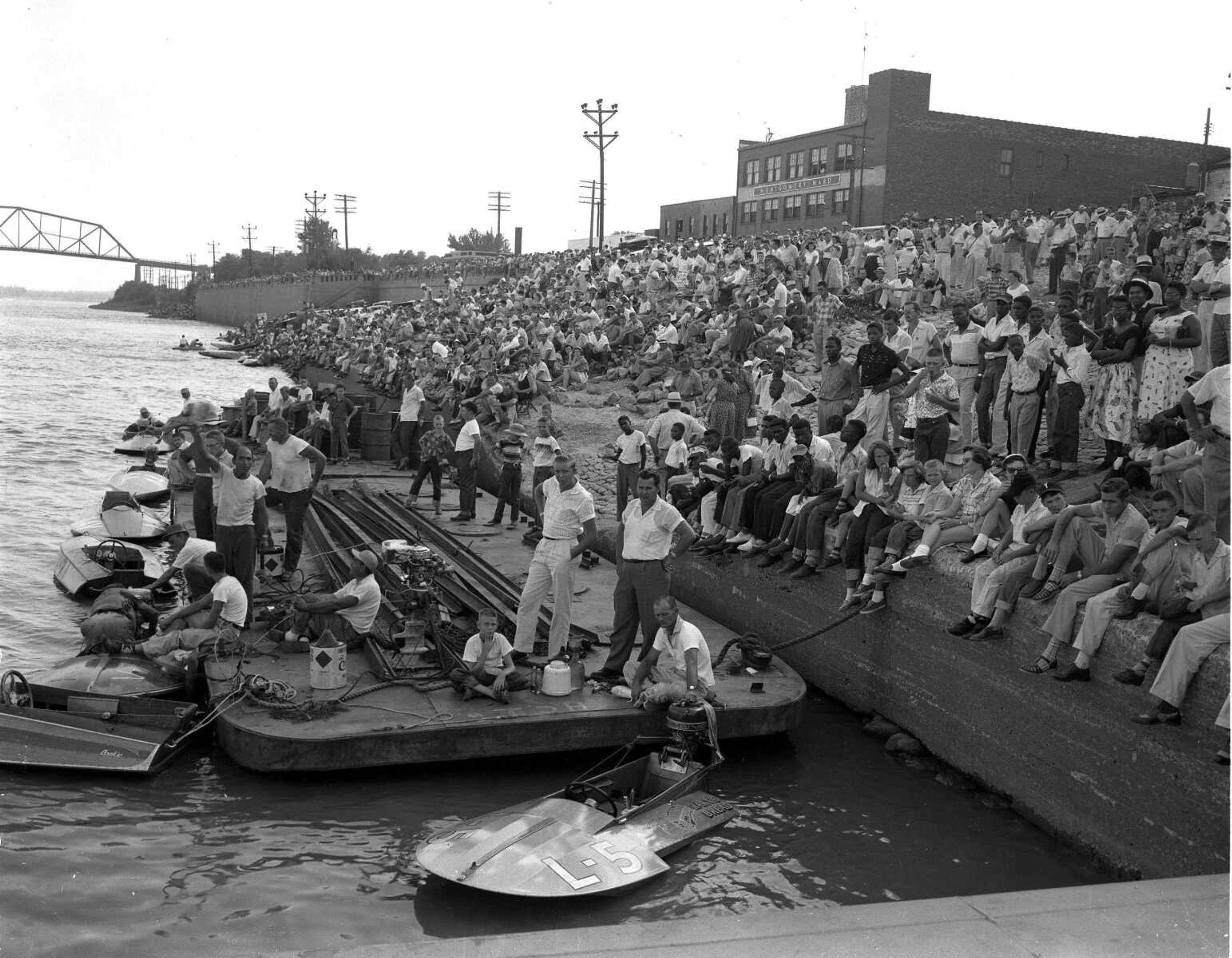 Published Monday, Aug. 15, 1955
A part of the thousands who lined the waterfront Sunday afternoon to witness the Missouri championship motorboat races. The picture looking south from the judges' stand located opposite the foot of Themis Street shows less than half of the crowd. In the foreground is shown one of the barges which served as a pit, out of which the racing boat drivers operated. Although the sun shone warmly, a brisk northern breeze made the temperature, for the most part, quite comfortable.
(Missourian archives photo by G.D. "Frony" Fronabarger)