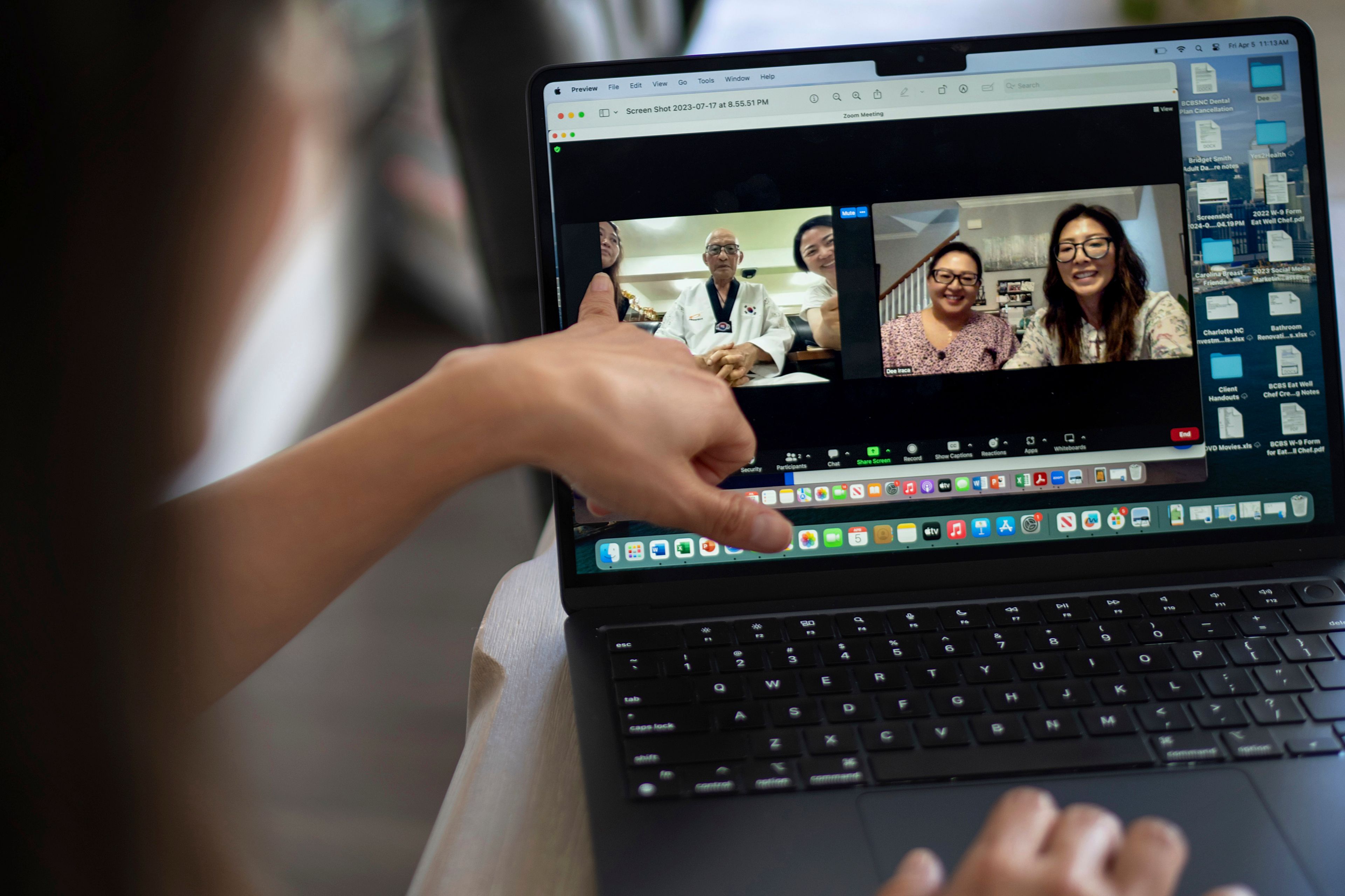 Dee Iraca, at her home in Davidson, N.C., on Friday, April 5, 2024, shows a video of a 2023 video call with her biological father, Park Jong-kyun. She points to fellow adoptee Rebecca Kimmel, left, who sat next to Park in South Korea as Iraca, seen in the window at far right, sits with her twin sister, Becca Webster, back in America. (AP Photo/David Goldman)