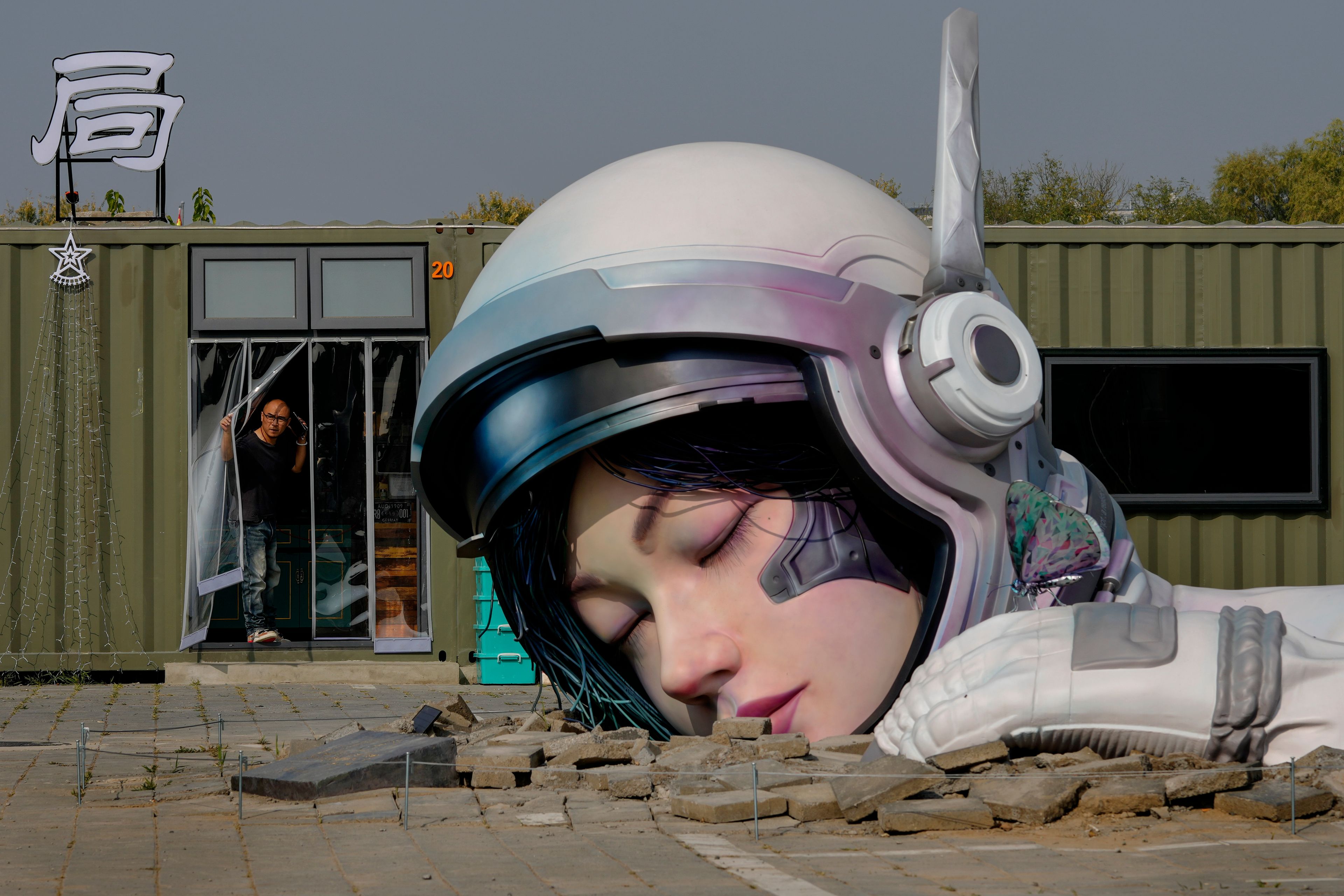 A man looks out from a container restaurant near an art sculpture depicting a sleeping Chinese astronaut in the Songzhuang art district in eastern Beijing, Tuesday, Oct. 29, 2024. (AP Photo/Andy Wong)