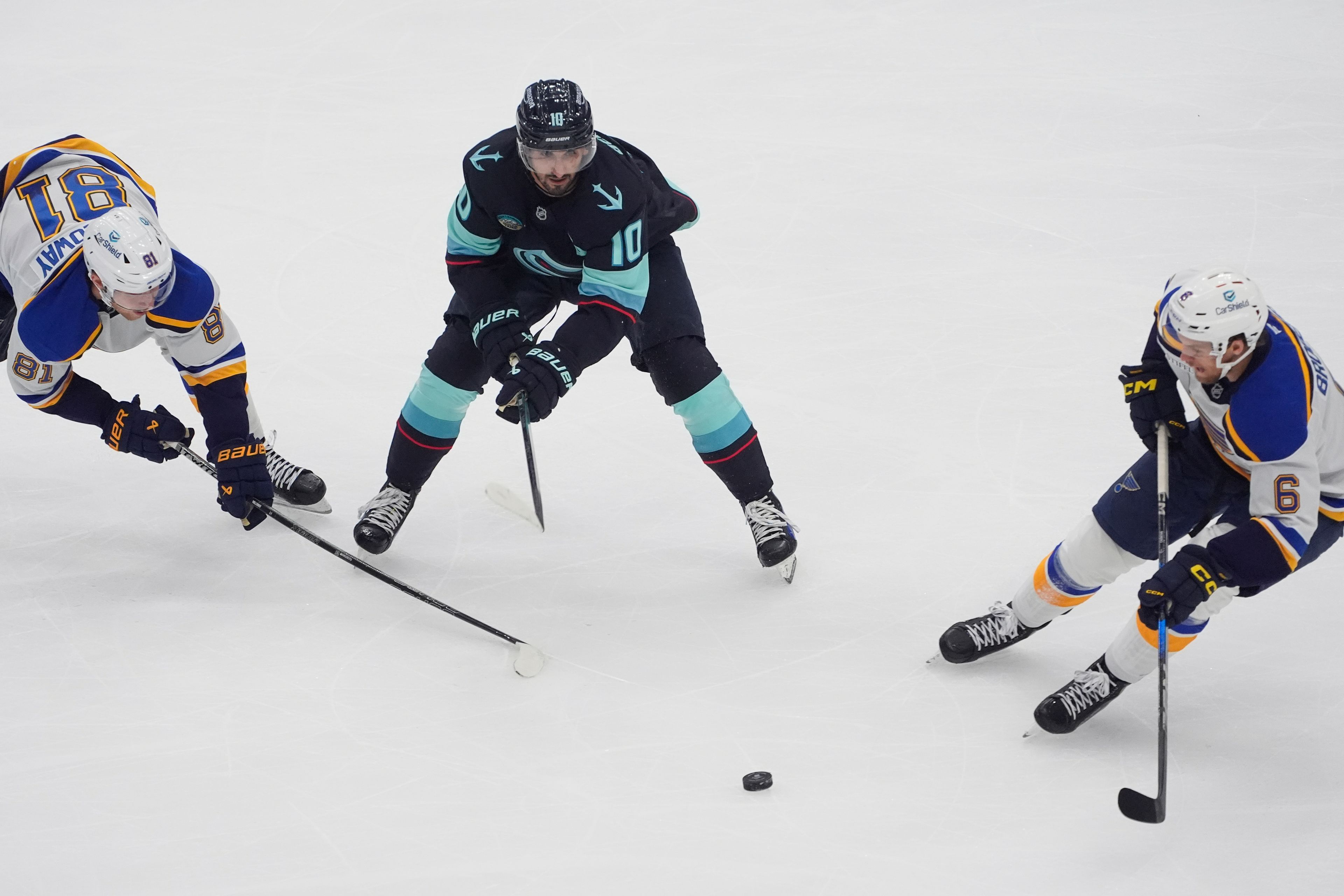 Seattle Kraken center Matty Beniers (10) looks on with St. Louis Blues center Dylan Holloway (81) as defenseman Philip Broberg (6) receives the puck during the first period of an NHL hockey game Tuesday, Oct. 8, 2024, in Seattle. (AP Photo/Lindsey Wasson)