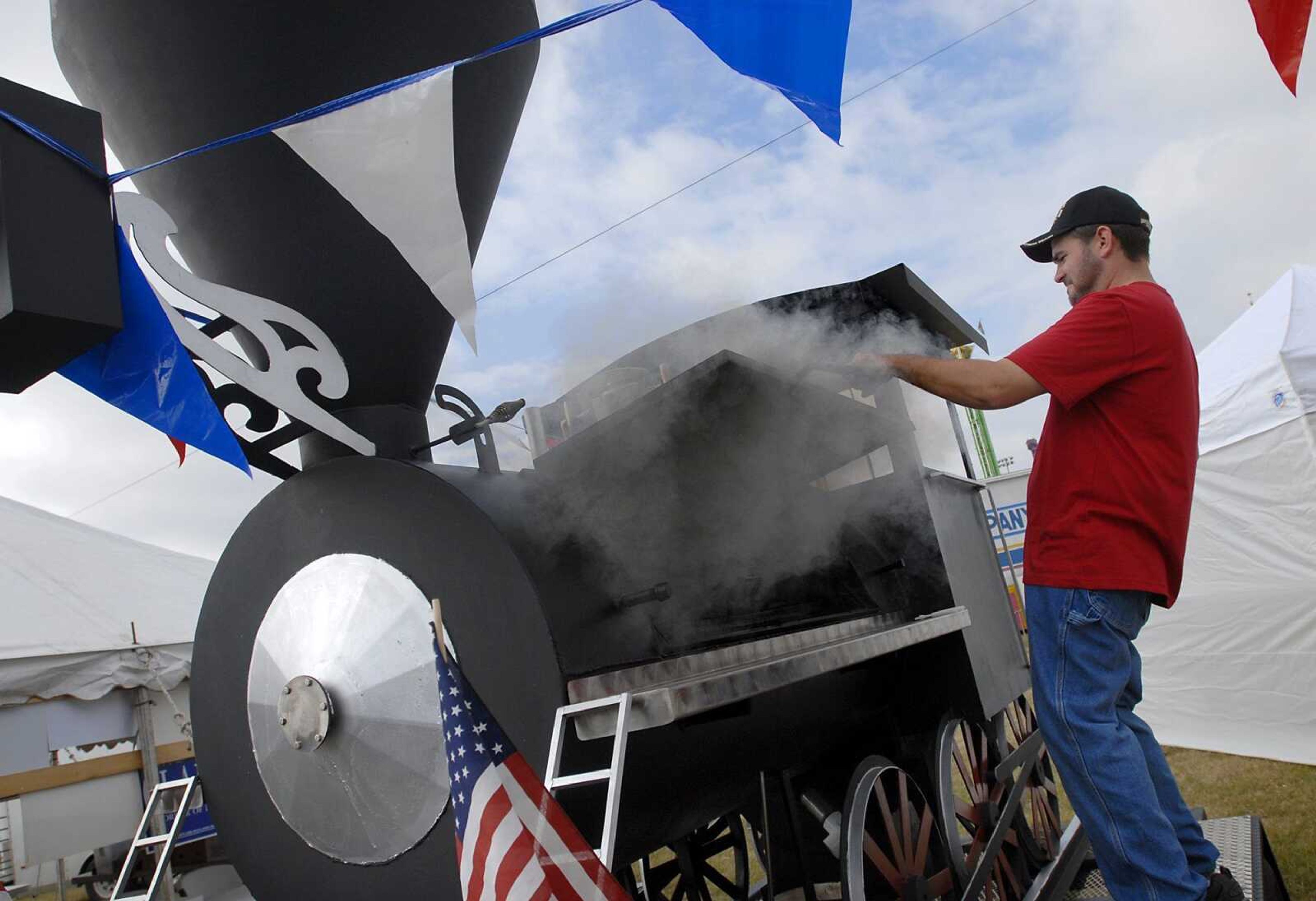 Patrick Moore, of D-Rails BBQ, checks on the burgers and hot dogs in a train-shaped grill at the SEMO District Fair on Saturday. This is the first year that D-Rails has opened a food booth at the fair. (Kristin Eberts)