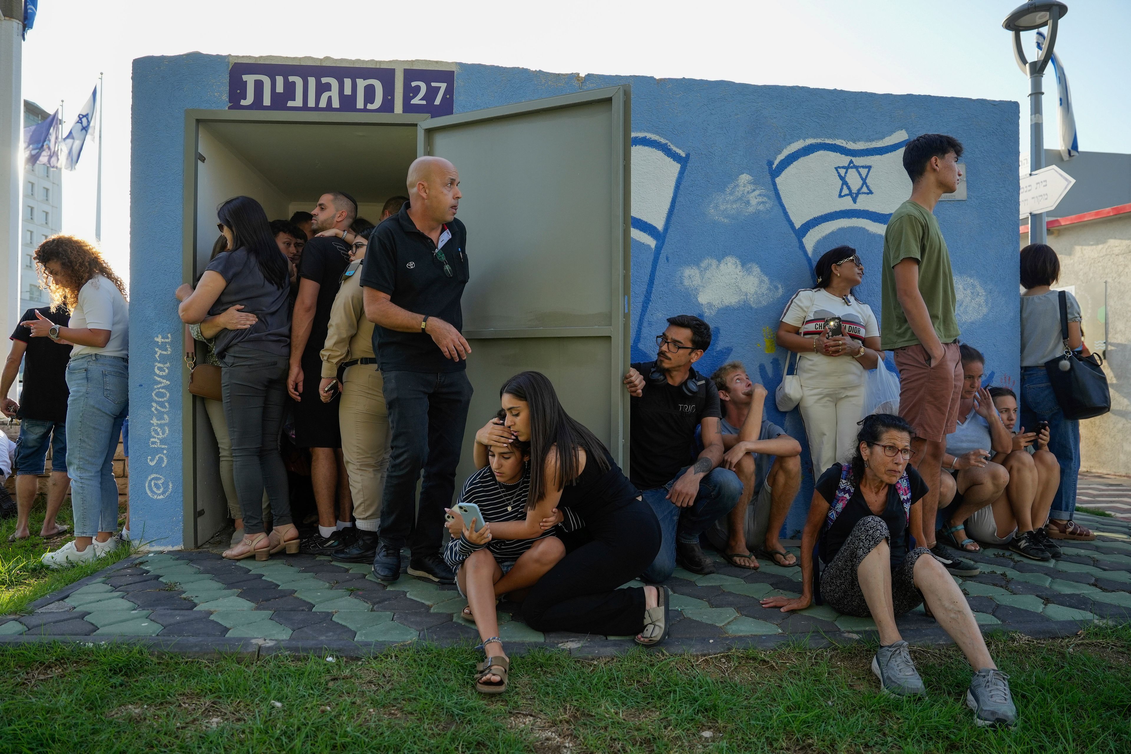 Israelis take cover next to a shelter as a siren sounds a warning of incoming rockets fired from Lebanon, in Nahariya, northern Israel, Thursday, Sept. 19, 2024. (AP Photo/Baz Ratner)