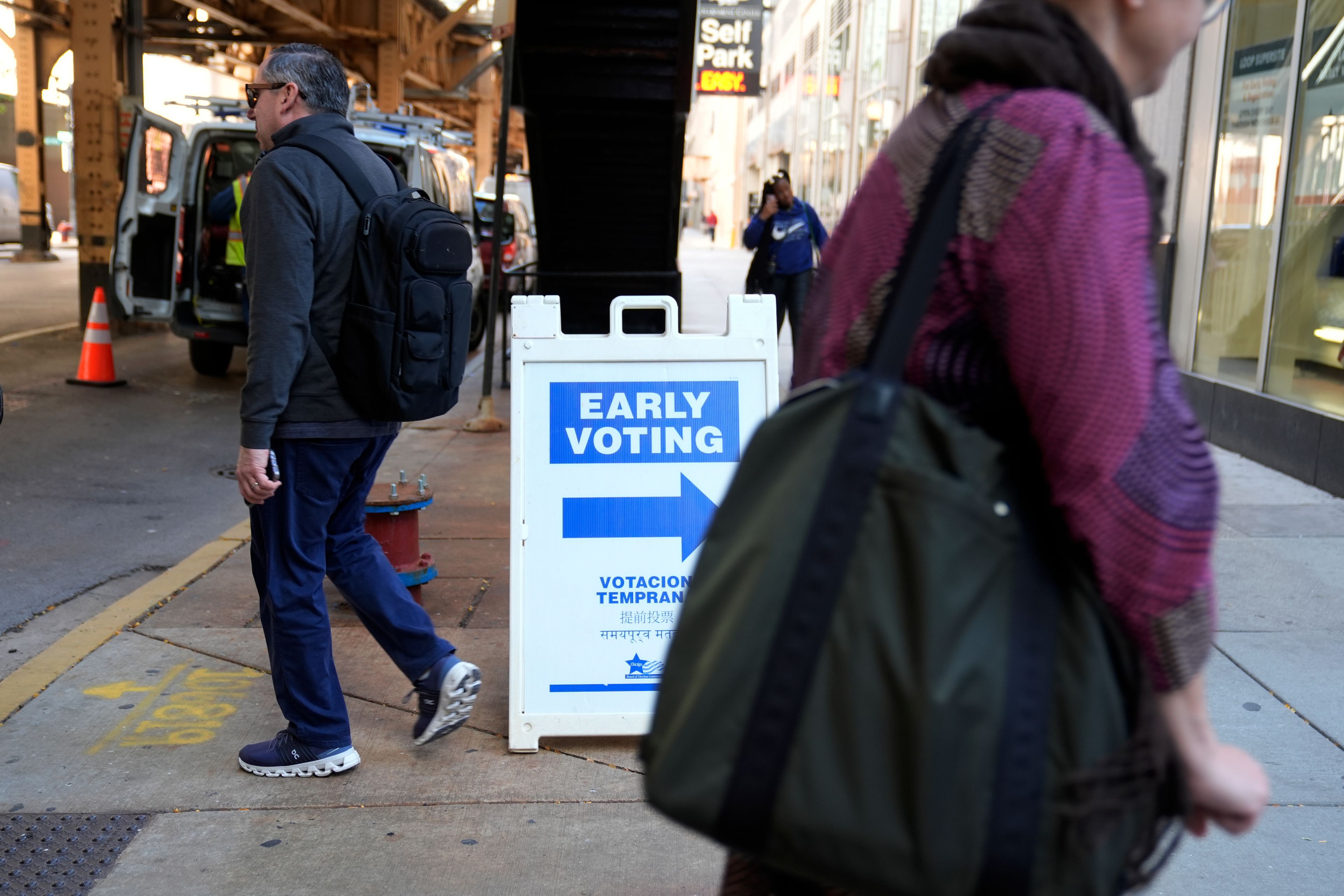 People walk by an early voting sign on the first day of early voting for the 2024 Presidential General Election, Thursday, Oct. 3, 2024 in Chicago. (AP Photo/Charles Rex Arbogast)