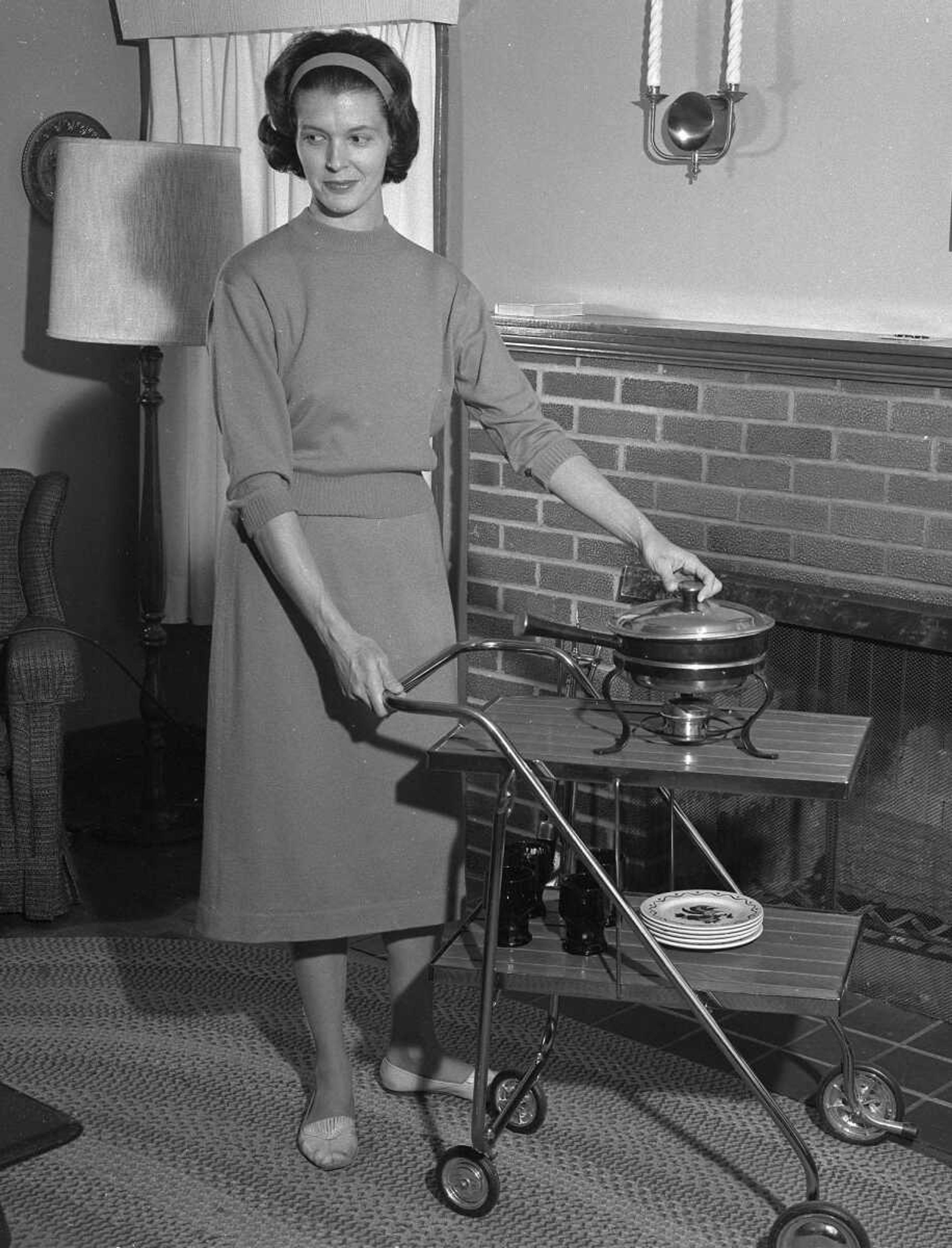 Published Dec. 28, 1963: Mrs. Sam Trainum demonstrates how she probably will serve her birthday dinner. Because her day and New Year's Day are one and the same, the living room, where the television set is, usually becomes the birthday dining room. Sometimes she has gone out for dinner, she says, but not when she has had a small baby. Julie, born Nov. 1, is her fourth child.