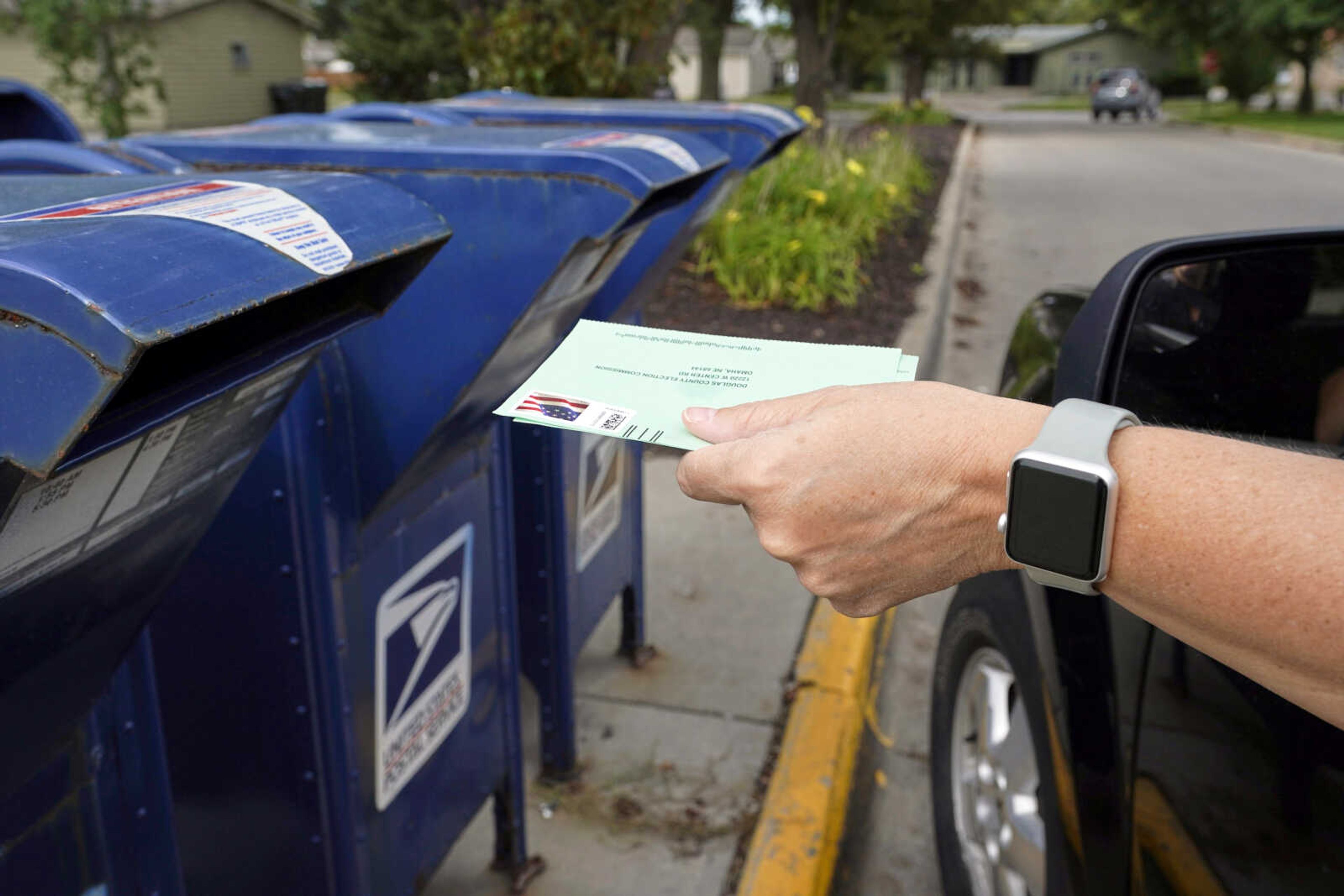 A person drops applications for mail-in ballots into a mail box Tuesday in Omaha, Nebraska. U.S. Postal Service warnings that it can't guarantee ballots sent by mail will arrive on time have put a spotlight on the narrow timeframes most states allow to request and return those ballots.