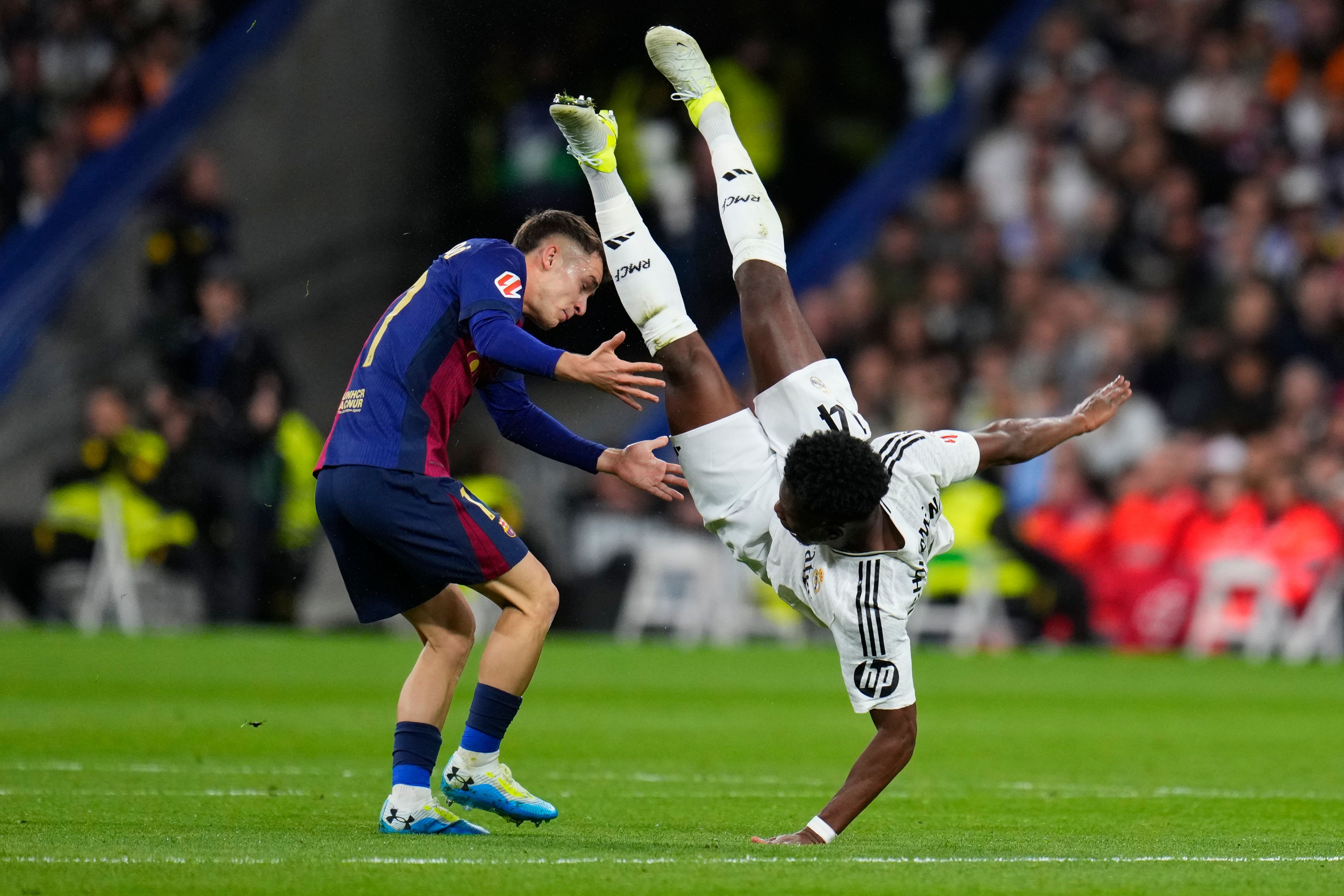 Real Madrid's Aurelien Tchouameni, right, falls next to Barcelona's Marc Casado during a Spanish La Liga soccer match between Real Madrid and Barcelona at the Santiago Bernabeu stadium in Madrid, Spain, Saturday, Oct. 26, 2024. (AP Photo/Manu Fernandez)