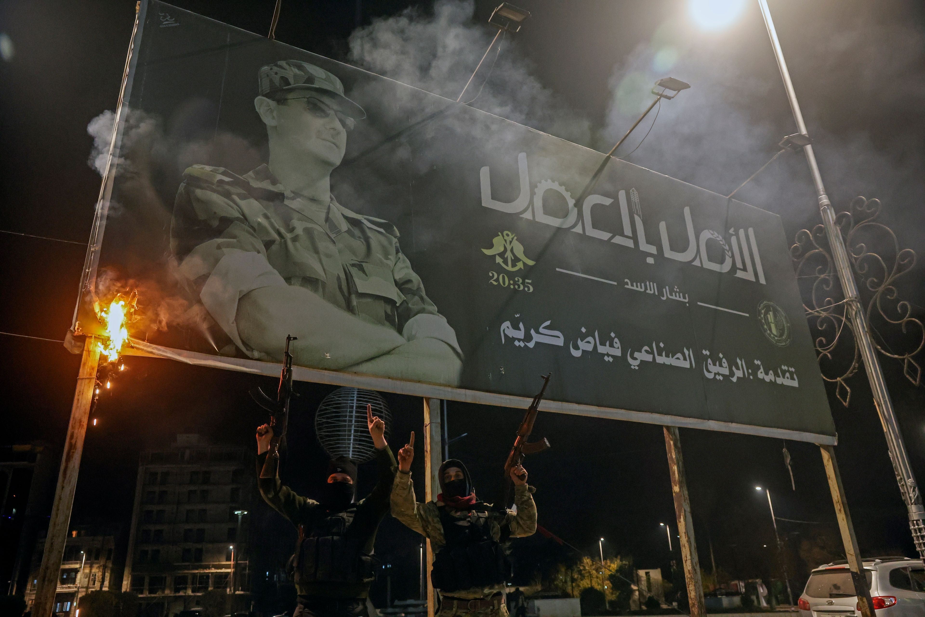 Opposition fighters hold up their guns as they pose for photos under a billboard depicting Syrian President Bashar Assad in Aleppo, Syria, late Friday, Nov. 29, 2024. (AP Photo/Ghaith Alsayed)