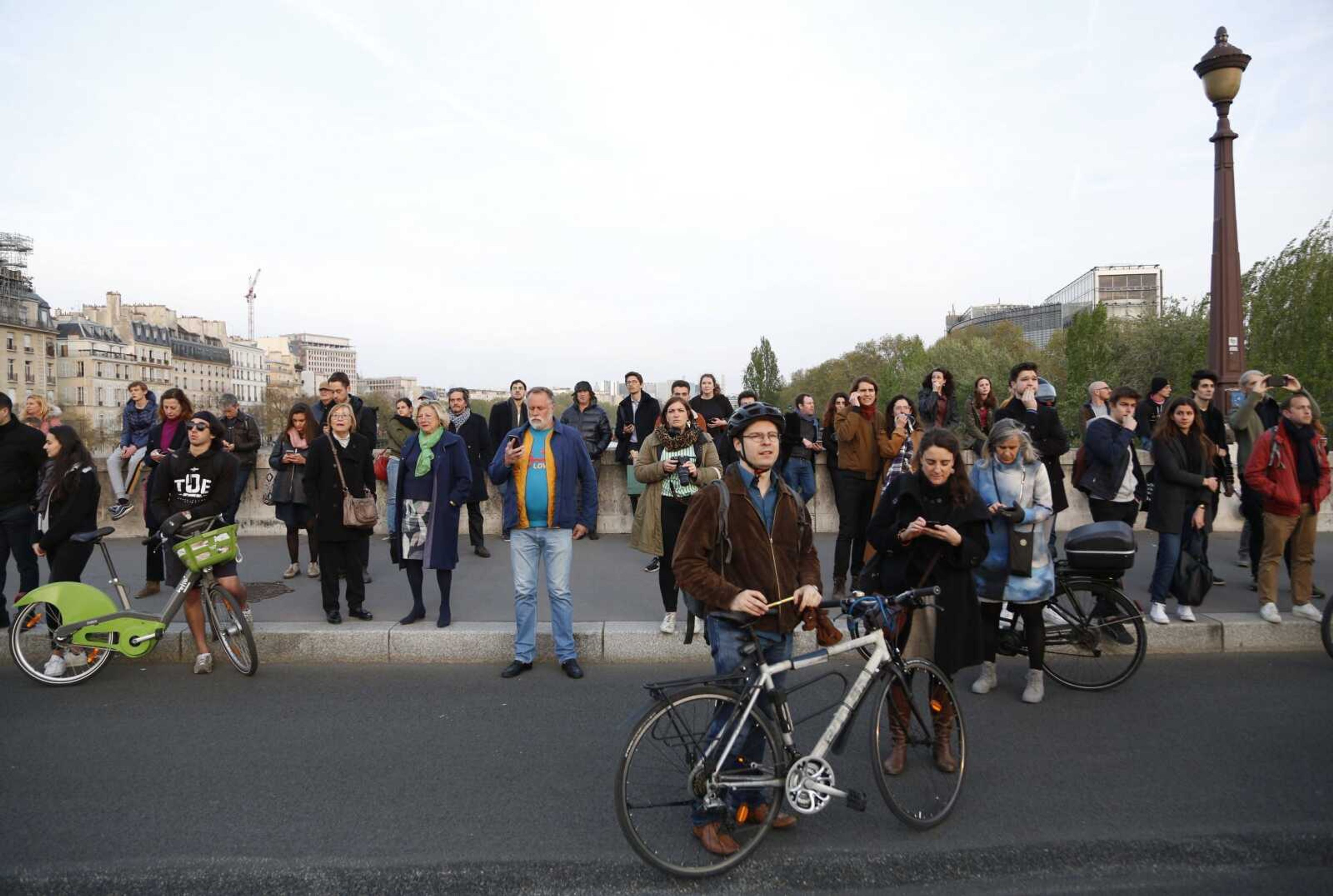 People watch as flames and smoke rise from Notre Dame cathedral as it burns in Paris, Monday, April 15, 2019. Massive plumes of yellow brown smoke is filling the air above Notre Dame Cathedral and ash is falling on tourists and others around the island that marks the center of Paris. (AP Photo/Thibault Camus)