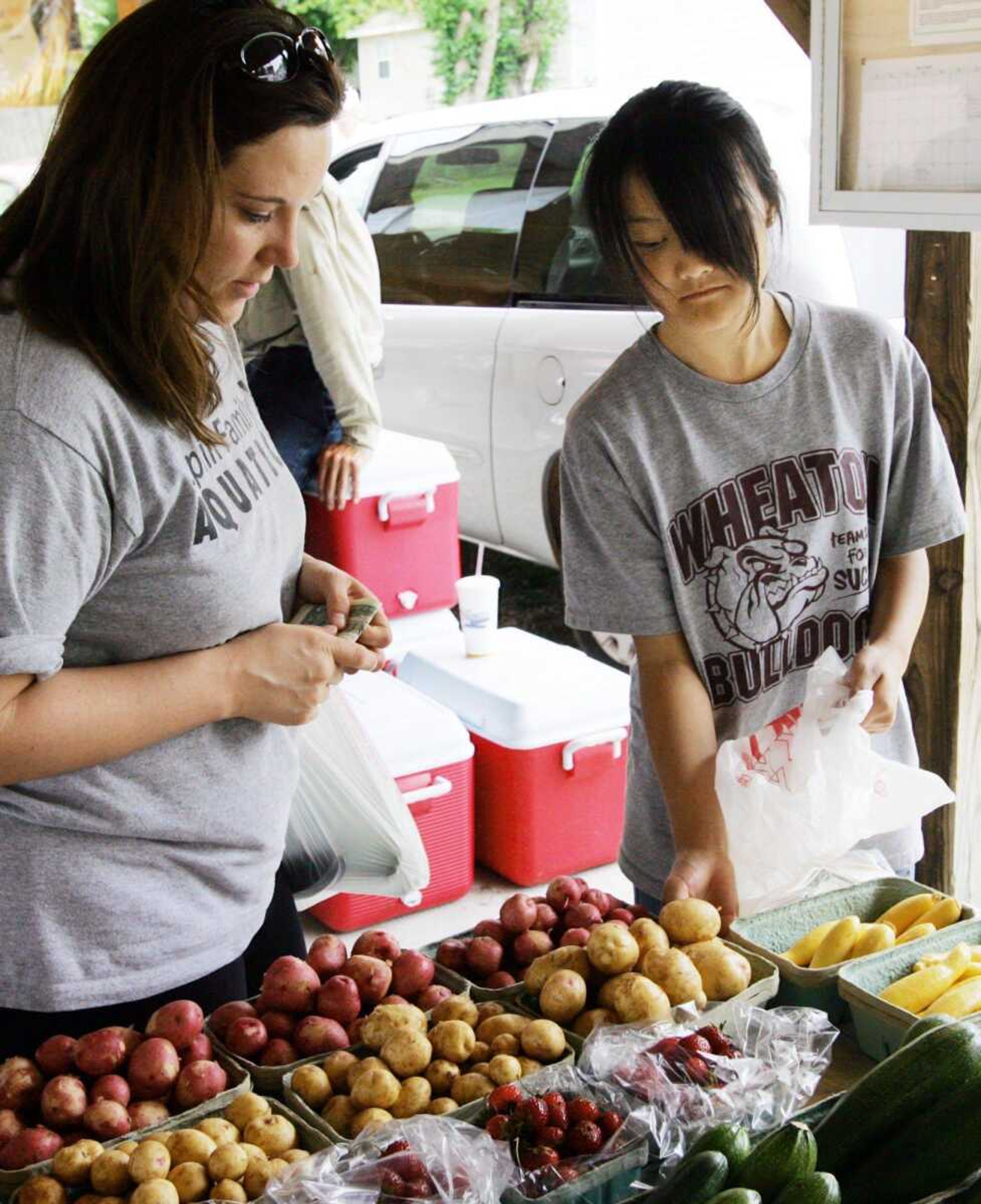 Brandi Johnson of Webb City, Mo., left purchases produce from Shing Lee, of Fairview, Mo., on May 26 at the Webb City Farmers Market in Webb City. Through a University of Missouri extension program, Asian farmers are learning how to grow American crops. (T. Rob Brown ~ The Joplin Globe)