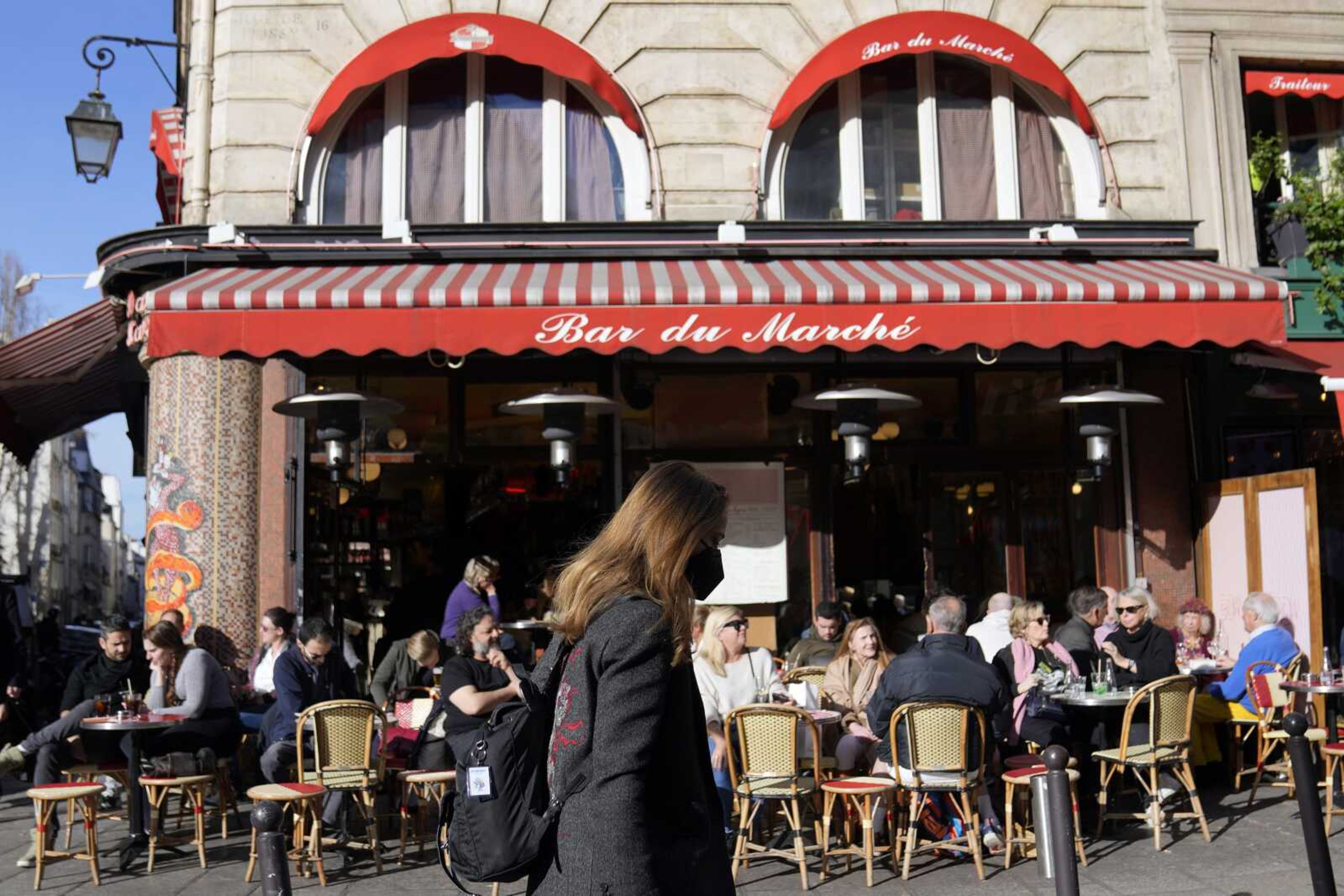 A woman wearing face mask walks in front of an open Parisian cafe March 14 in Paris. France and Germany have seen big spikes in COVID-19 infections in recent weeks, and the number of hospitalizations in the U.K. and France have climbed again.