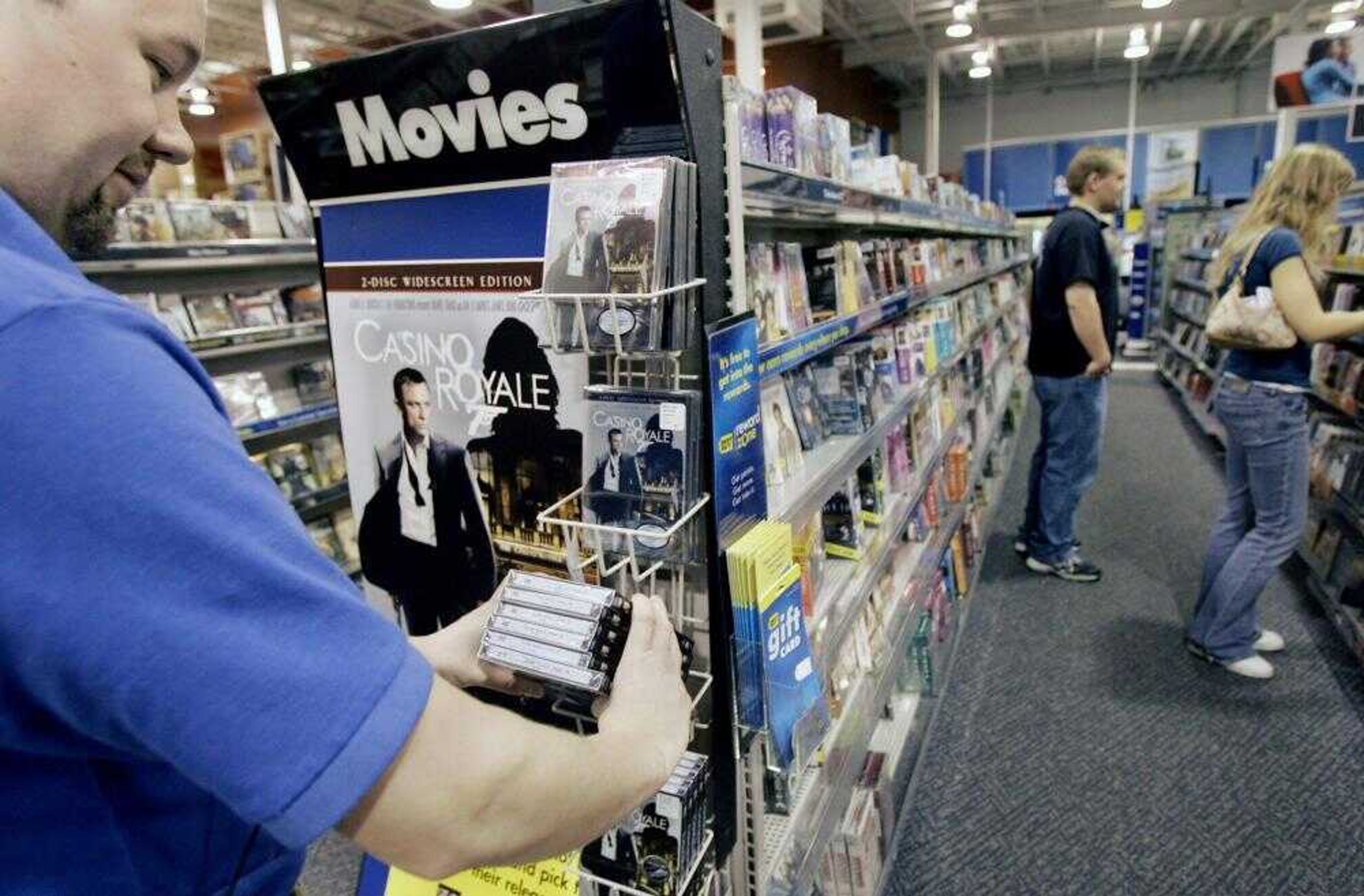 Shoppers looked at DVDs at a Best Buy store in Minnetonka, Minn., as employee James Hilgers, left, worked in the DVD section. Wal-Mart has launched its own movie download service, Best Buy is said to be in talks to start one, and Blockbuster explored buying movie download company Movielink earlier this year. (JIM MONE ~ Associated Press)