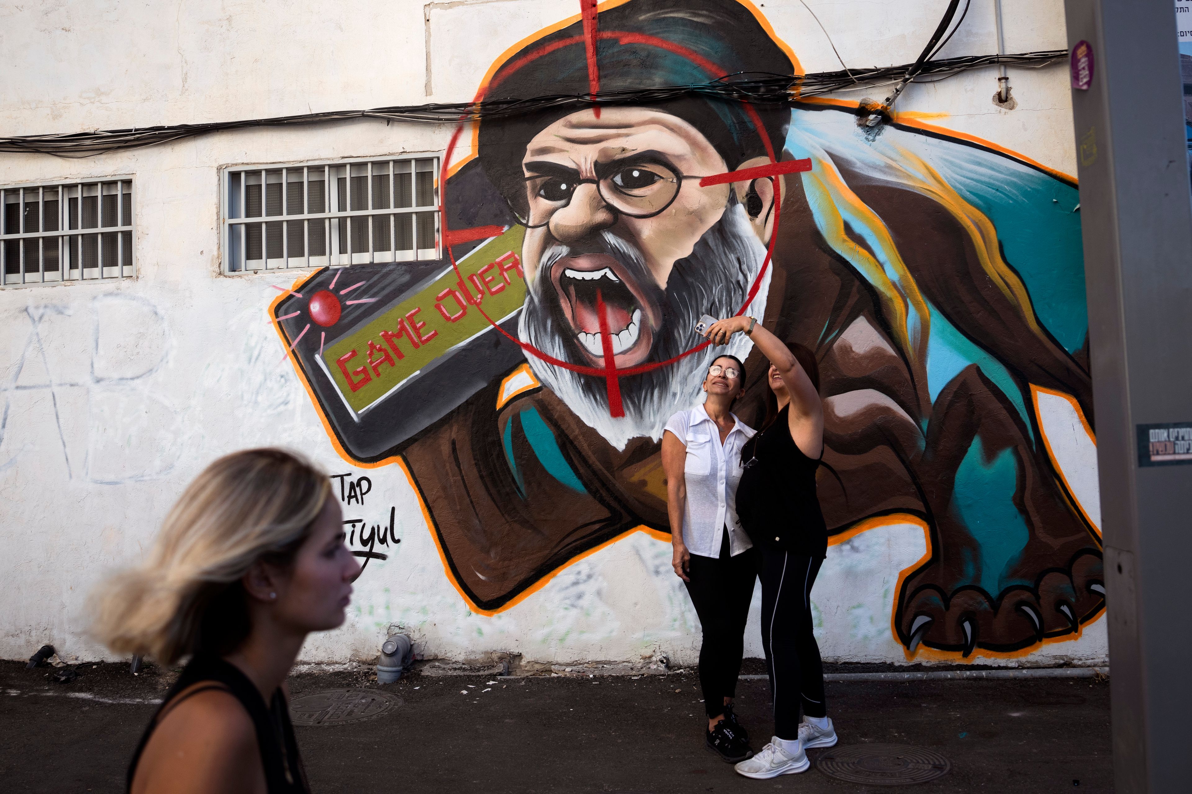 Two women take a selfie next to a newly painted graffiti of Hezbollah leader Hassan Nasrallah, a day after Hezbollah confirms its leader was killed in an Israeli airstrike, in Tel Aviv, Israel, on Sunday, Sept. 29, 2024. (AP Photo/Oded Balilty)