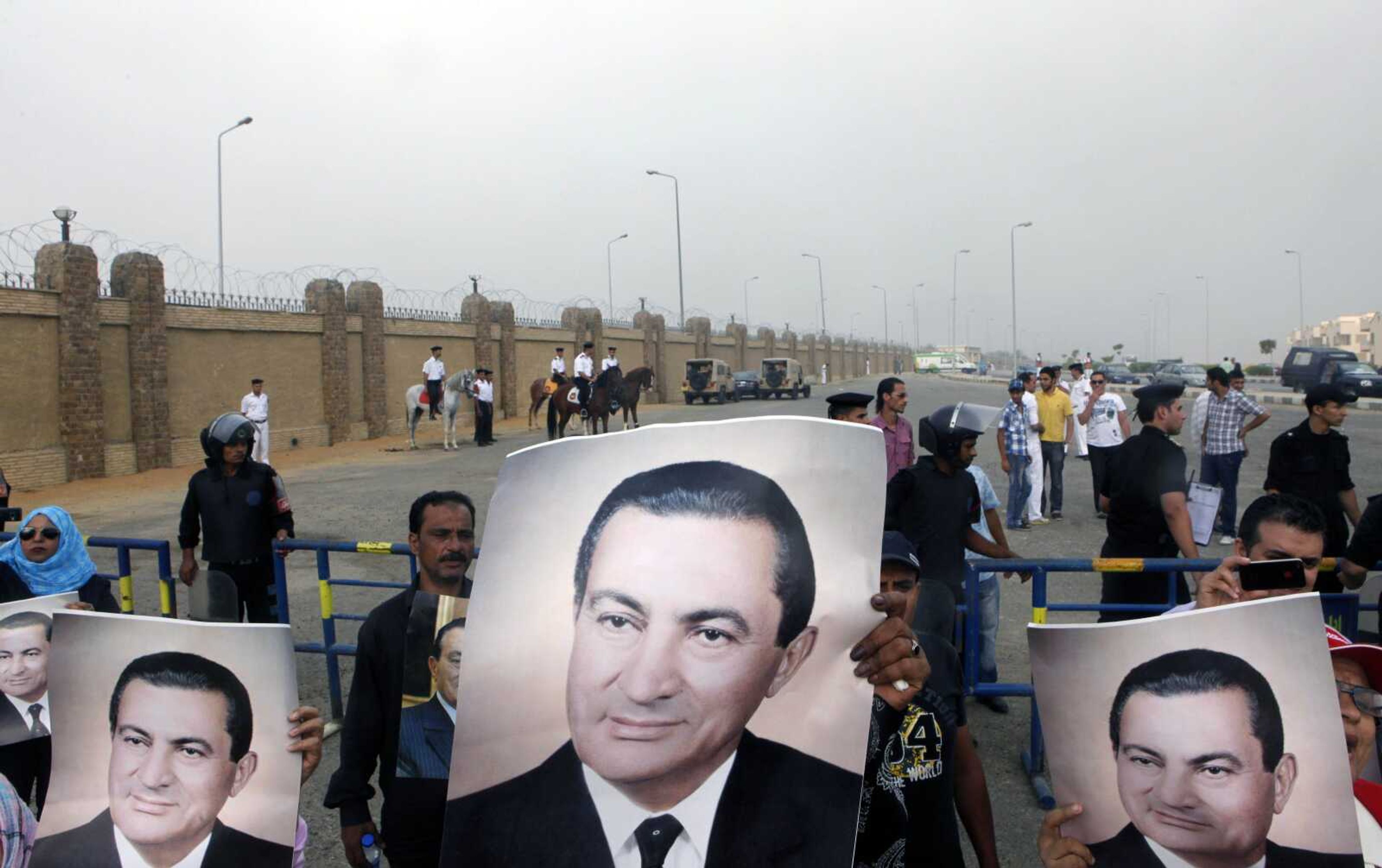 Egyptian pro-Mubarak supporters flash his posters Monday outside police academy court in Cairo. (Amr Nabil ~ Associated Press)