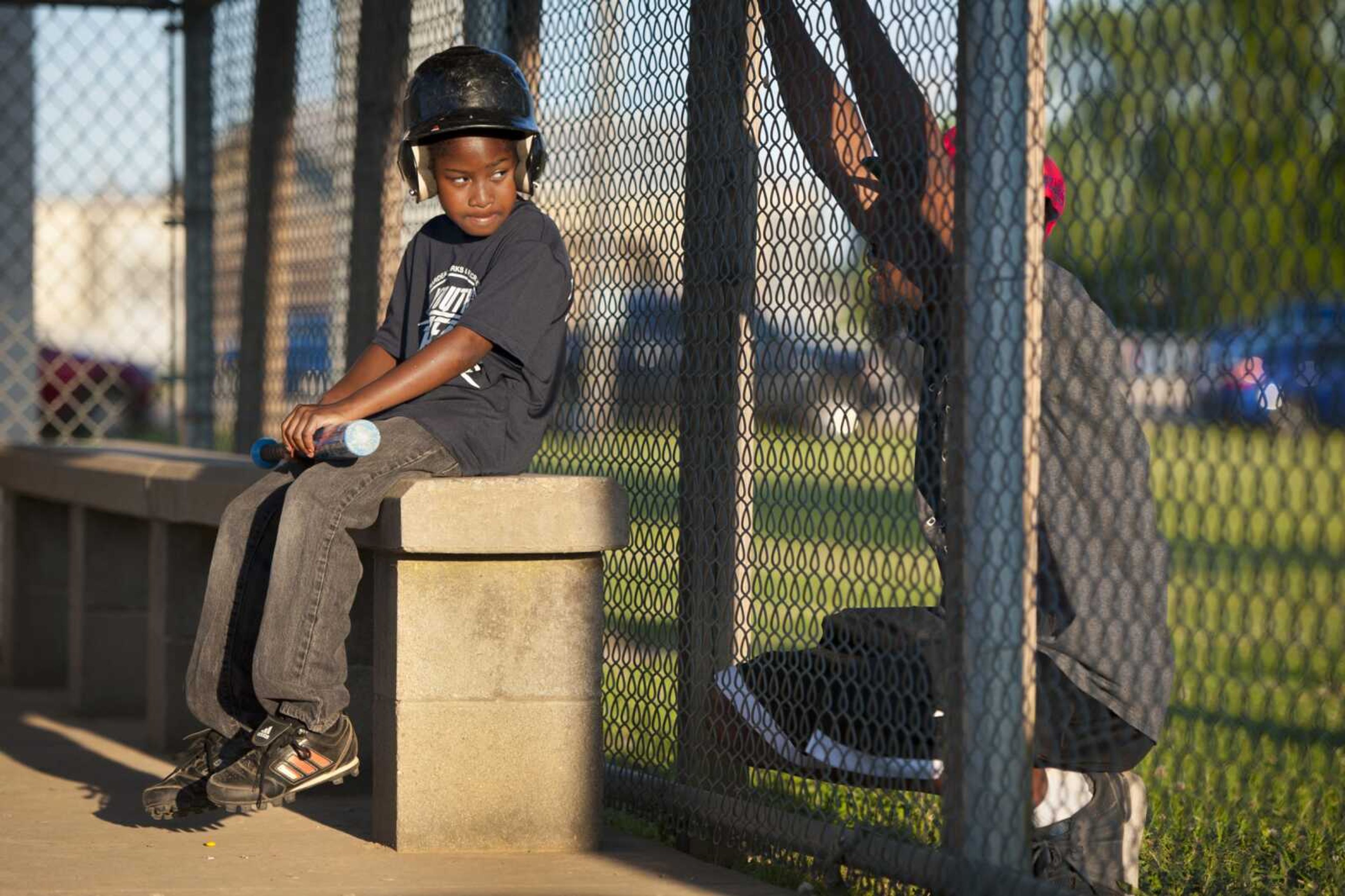 While waiting to bat during his first baseball game with an organized team, 9-year-old Damien Powell sits in the dugout at Arena Park Field 6 as his father, Darrell Powell, shares words of encouragement through a chain-link fence Tuesday, June 16, 2020, in Cape Girardeau.