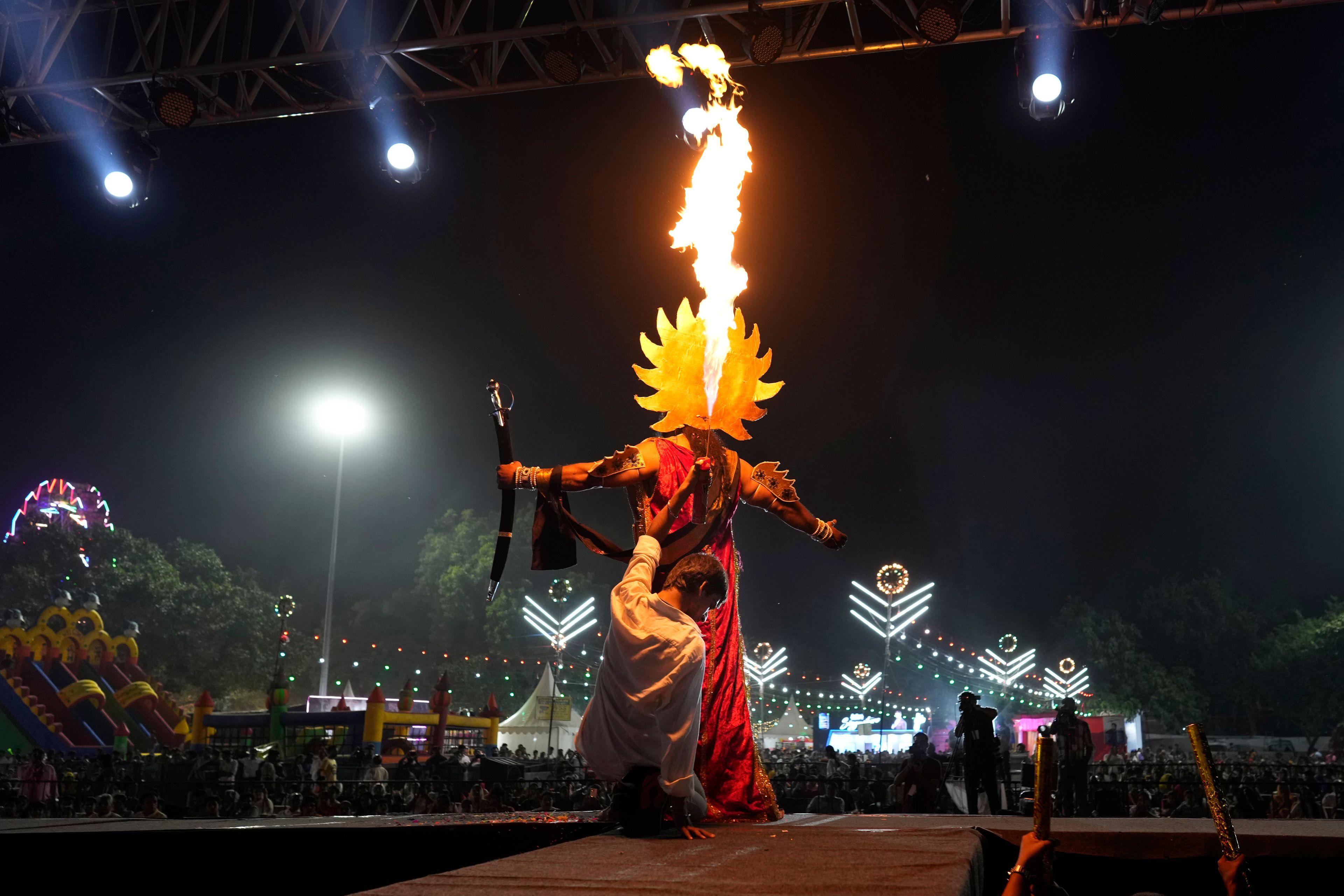 A production assistant holds a fire stick sitting behind Vikas Sirswal, 32, who is playing the demon king Ravana onstage, during Ramleela, a dramatic folk re-enactment of the life of Hindu god Rama according to the ancient Hindu epic Ramayana, in New Delhi,India, Wednesday, Oct. 9, 2024. (AP Photo/Manish Swarup)