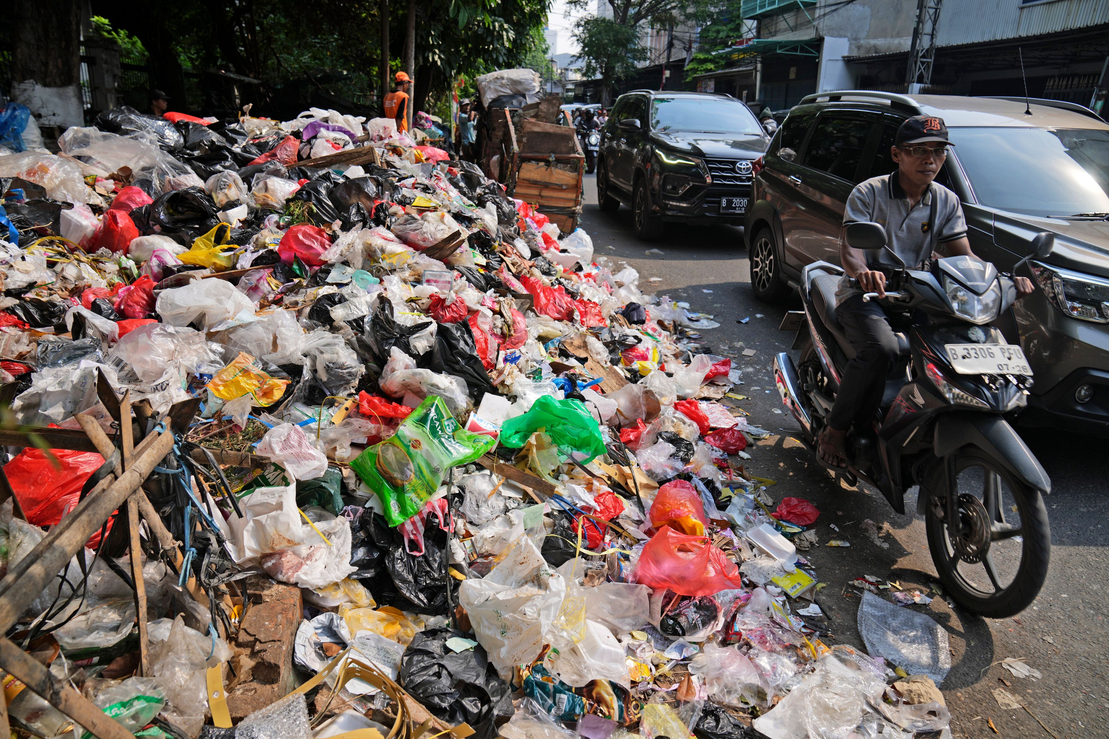 Motorists ride past garbage, most of them plastic, piled up on the side of a road in Jakarta, Indonesia, Tuesday, Nov. 26, 2024. (AP Photo/Dita Alangkara)