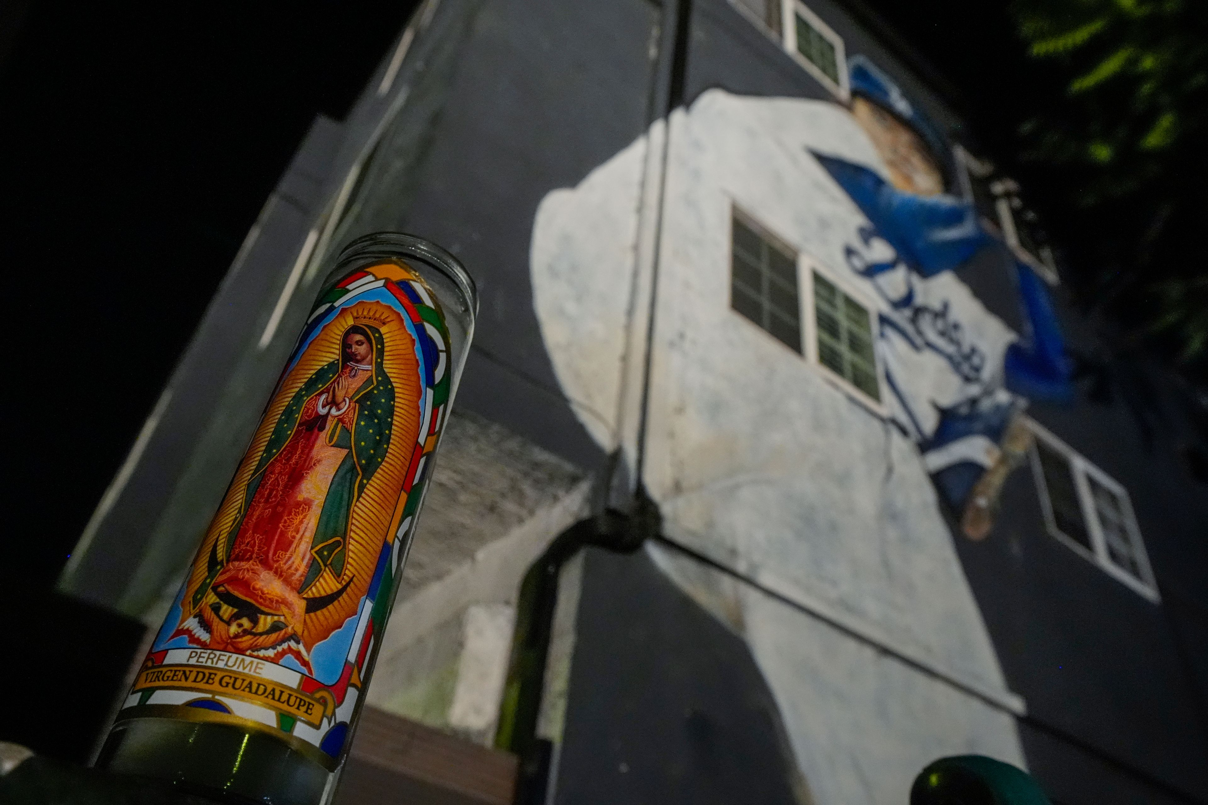 A votive candle donning an image of the Virgen de Guadalupe sits near a mural depicting former Los Angeles Dodgers pitcher Fernando Valenzuela, Tuesday, Oct. 22, 2024, in Los Angeles. (AP Photo/Julio Cortez)