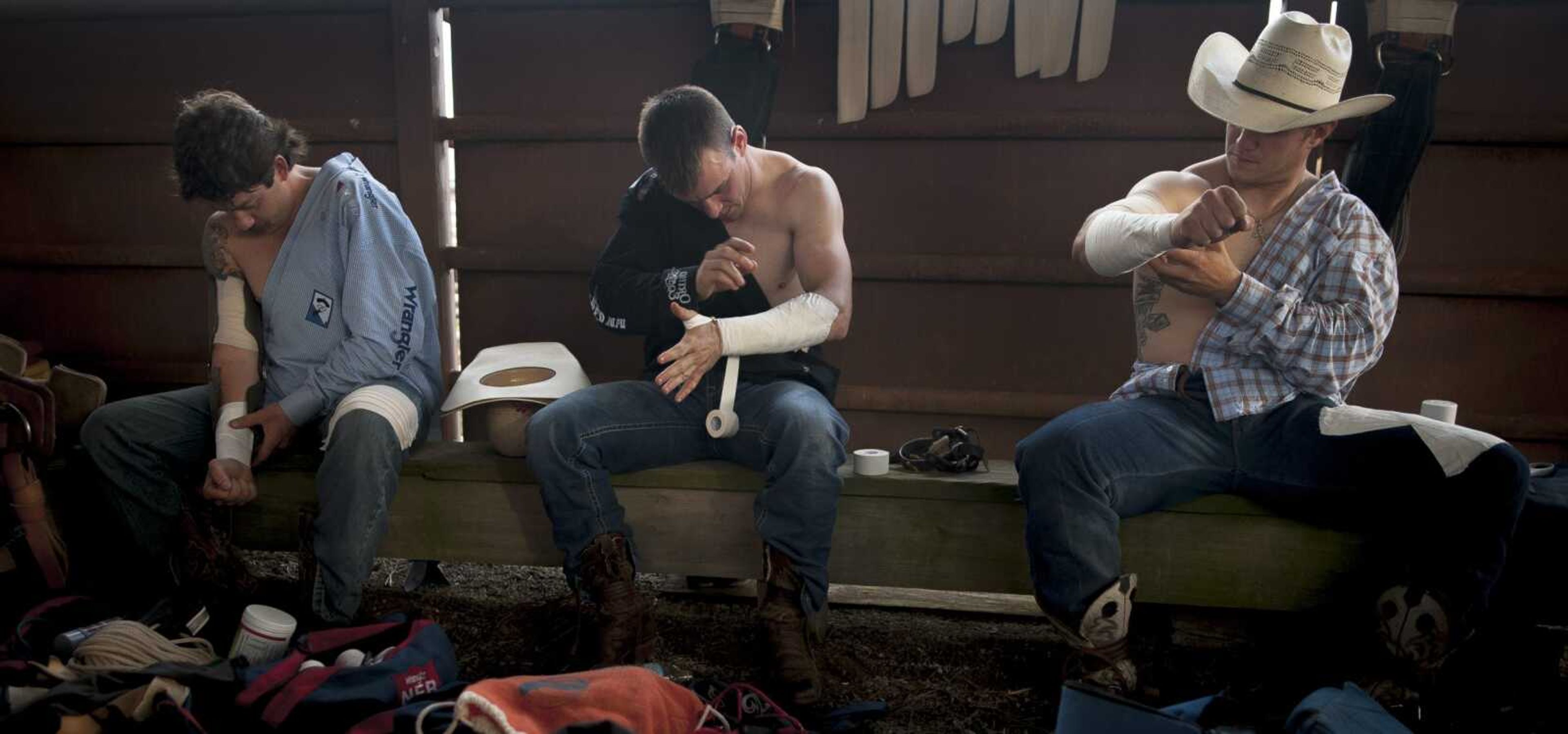 From left, Wyatt Denny, Tim O'Connell and Briar Dittmer tape their arms in preparation for riding in competition during the Sikeston Jaycee Bootheel Rodeo Wednesday, Aug. 7, 2019, in Sikeston.