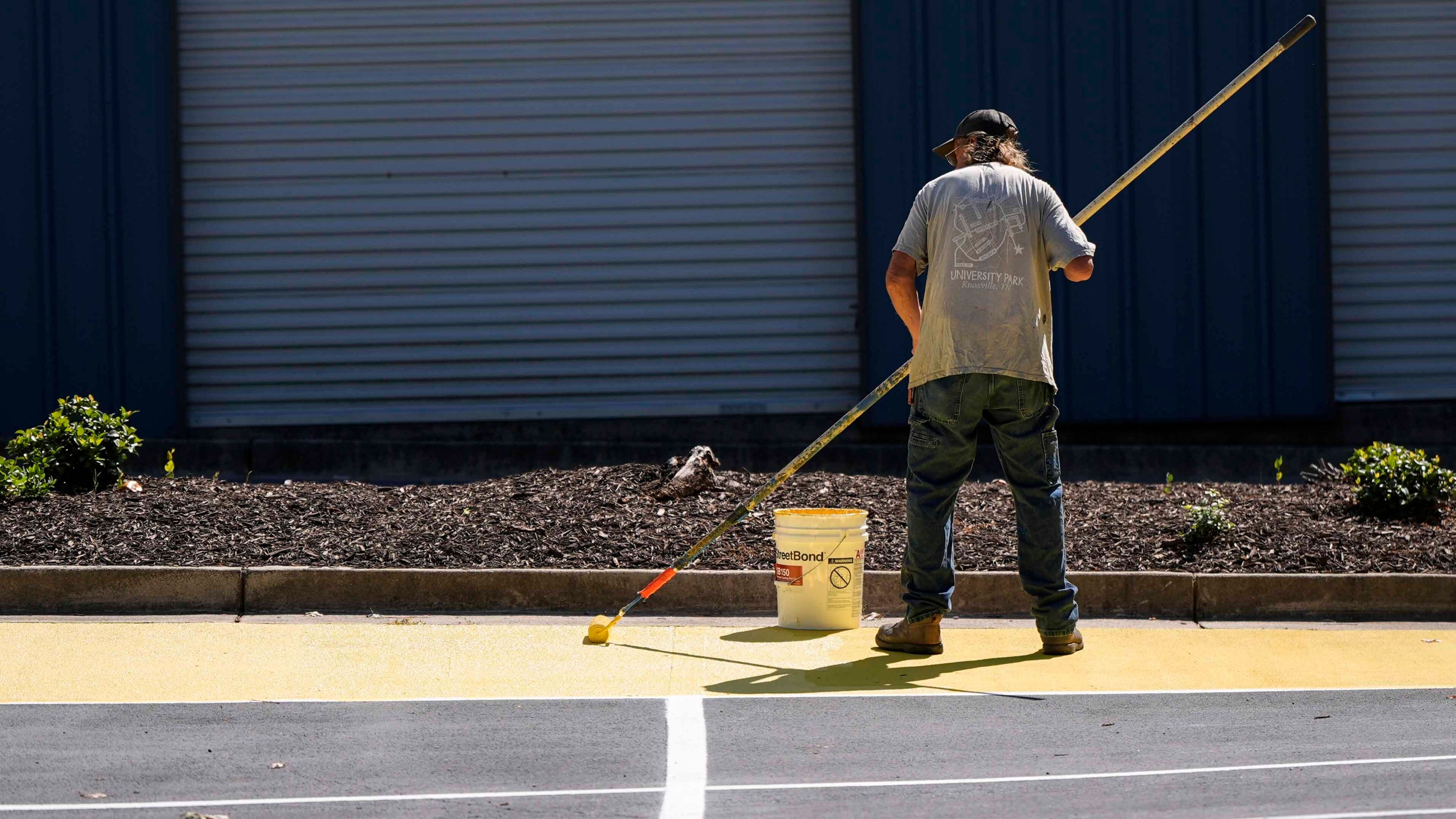 Ronnie Jefferies paints the parking lot at Science, Arts and Entrepreneurship School to help cool it by making it more reflective, Wednesday, Sept. 4, 2024, in Mableton, Ga. (AP Photo/Mike Stewart)