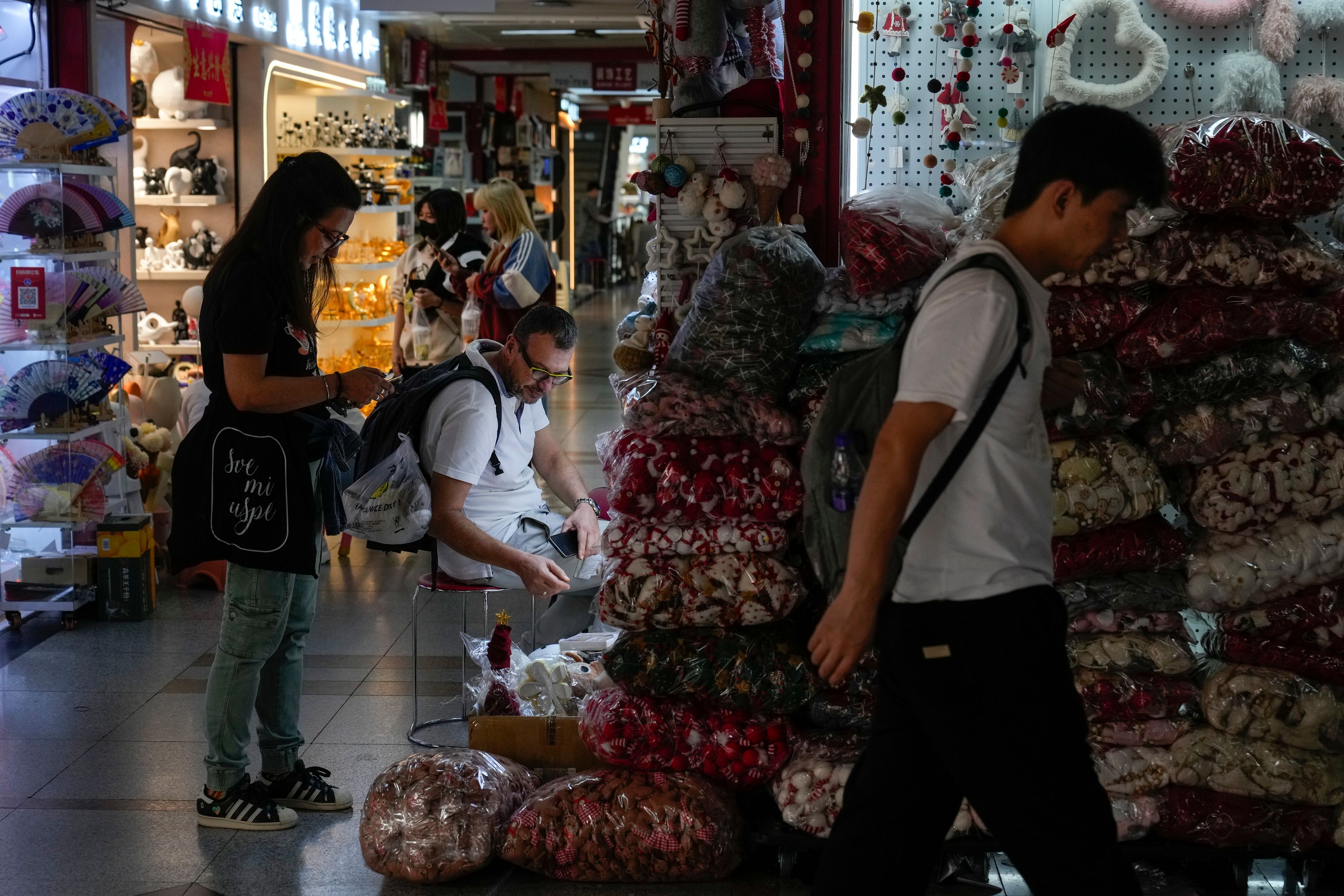 A man walks by foreign buyers shopping for Christmas decorations at the Yiwu wholesale market in Yiwu, east China's Zhejiang province on Nov. 8, 2024. (AP Photo/Andy Wong)