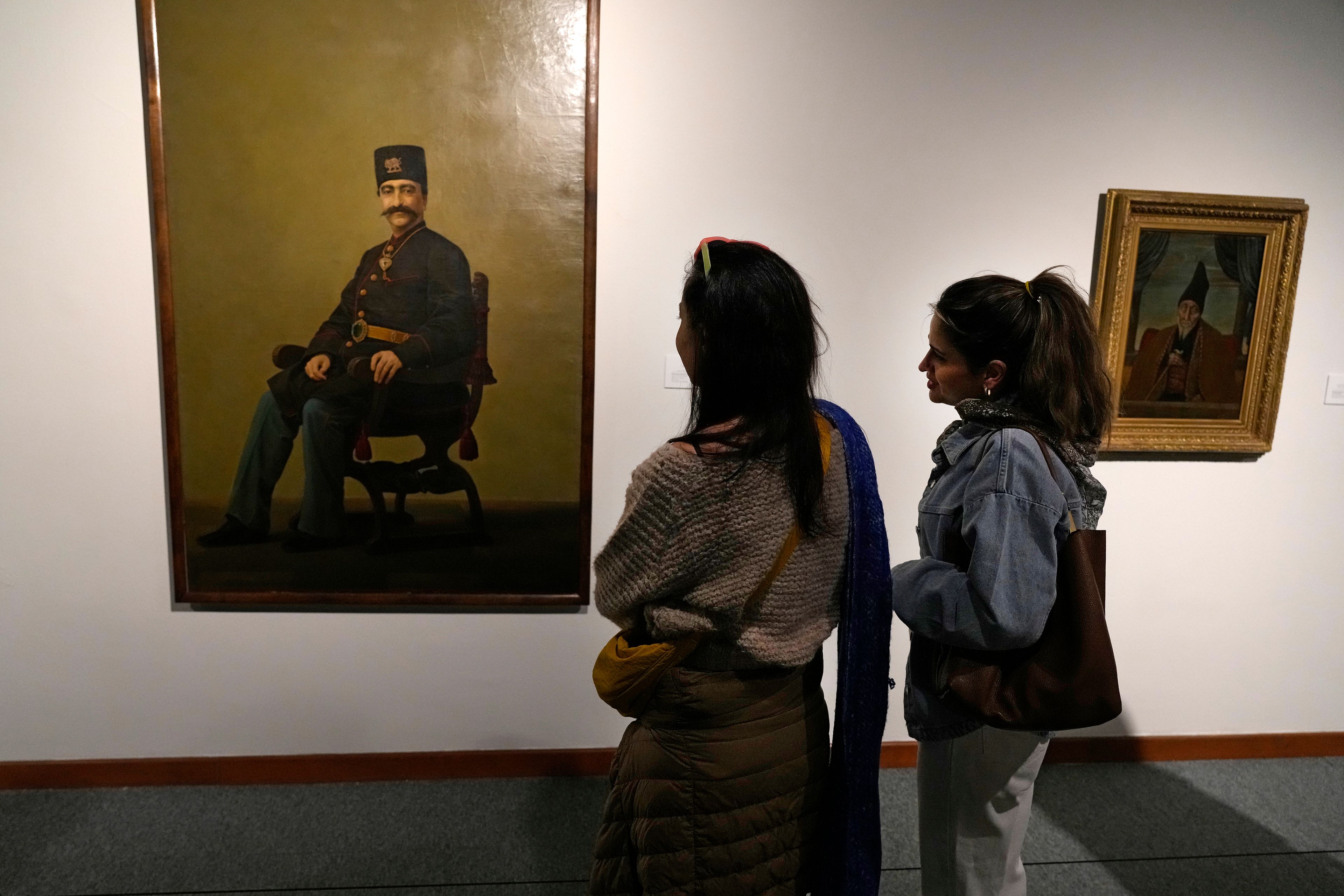 Two women look at a portrait of late Nasser-e-Din Shah, a king of Qajar dynesty, painted by Iranian painter Mohammad Ghaffari, also known as Kamal-ol-Molk, as they visit an exhibition titled Eye to Eye which showcases over 120 works by modern world artists as well as Iranian painters at Tehran Museum of Contemporary Art, in Tehran, Thursday, Nov. 21, 2024. (AP Photo/Vahid Salemi)