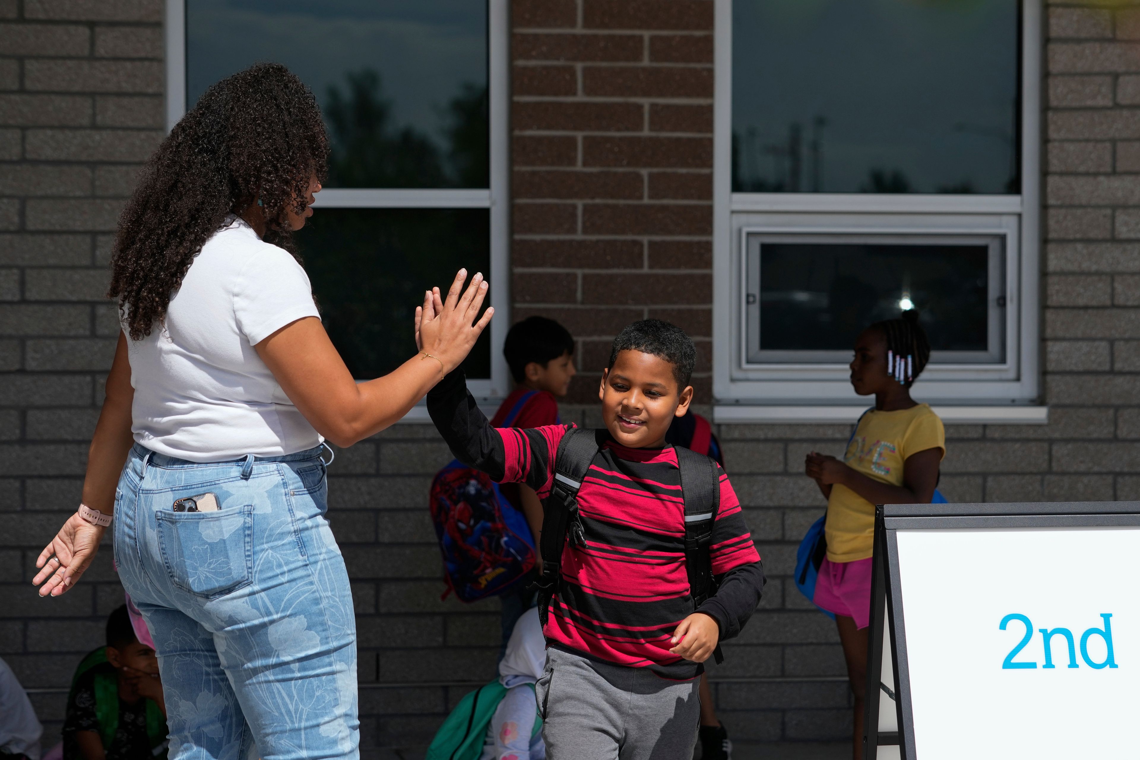 Dylan Martínez-Ramírez, center, high-fives his teacher Aliah James, left, after school Thursday, Aug. 29, 2024, in Aurora, Colo. (AP Photo/Godofredo A. Vásquez)