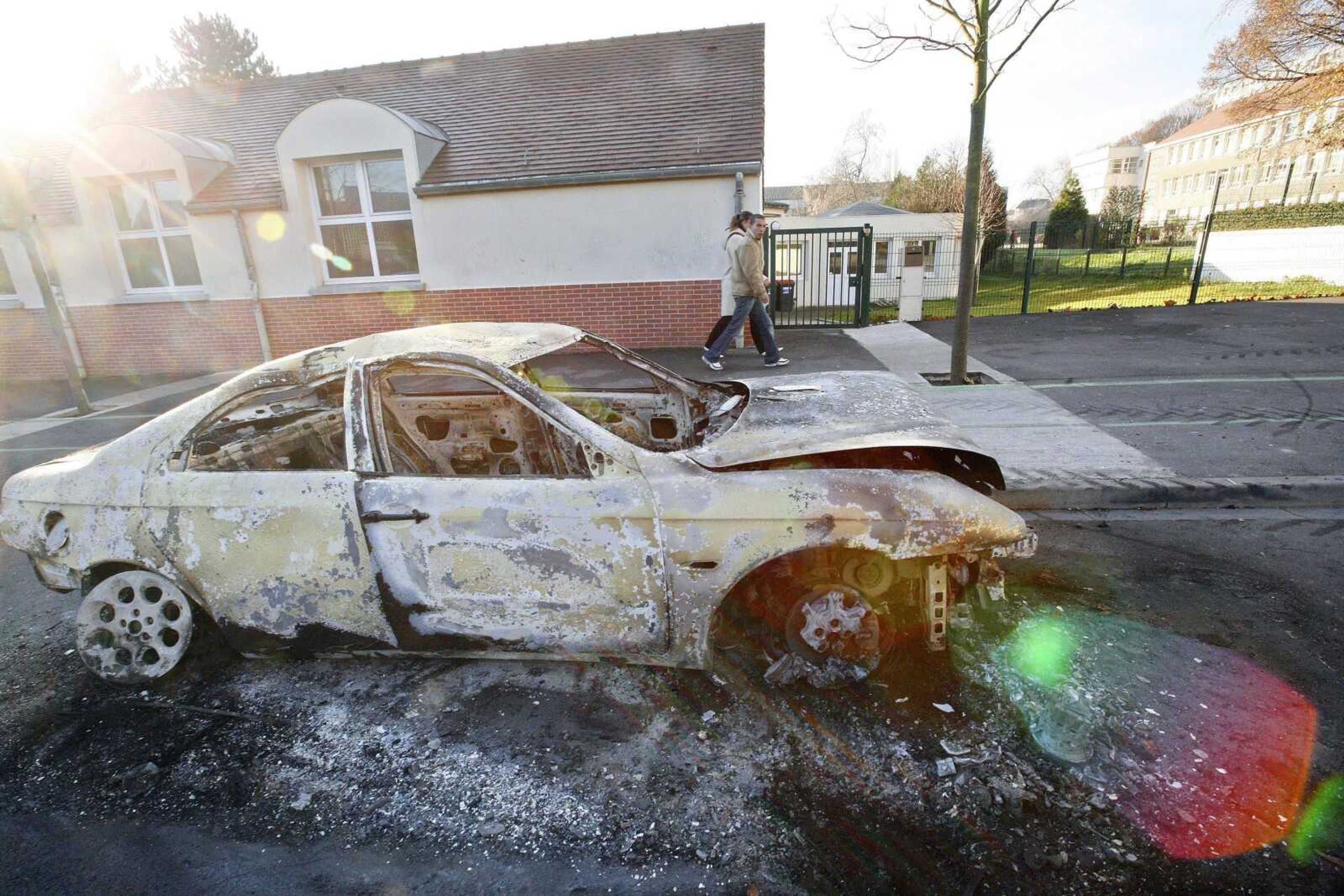 Residents walked past a car that was burned overnight during clashes between youths and police Tuesday in Villiers-le-Bel, a northern Paris suburb. Rioting in the tough suburbs of northern Paris took a dramatic and potentially deadly new turn with the use of firearms against police, officials said Tuesday. (Jacques Brinon ~ Associated Press)