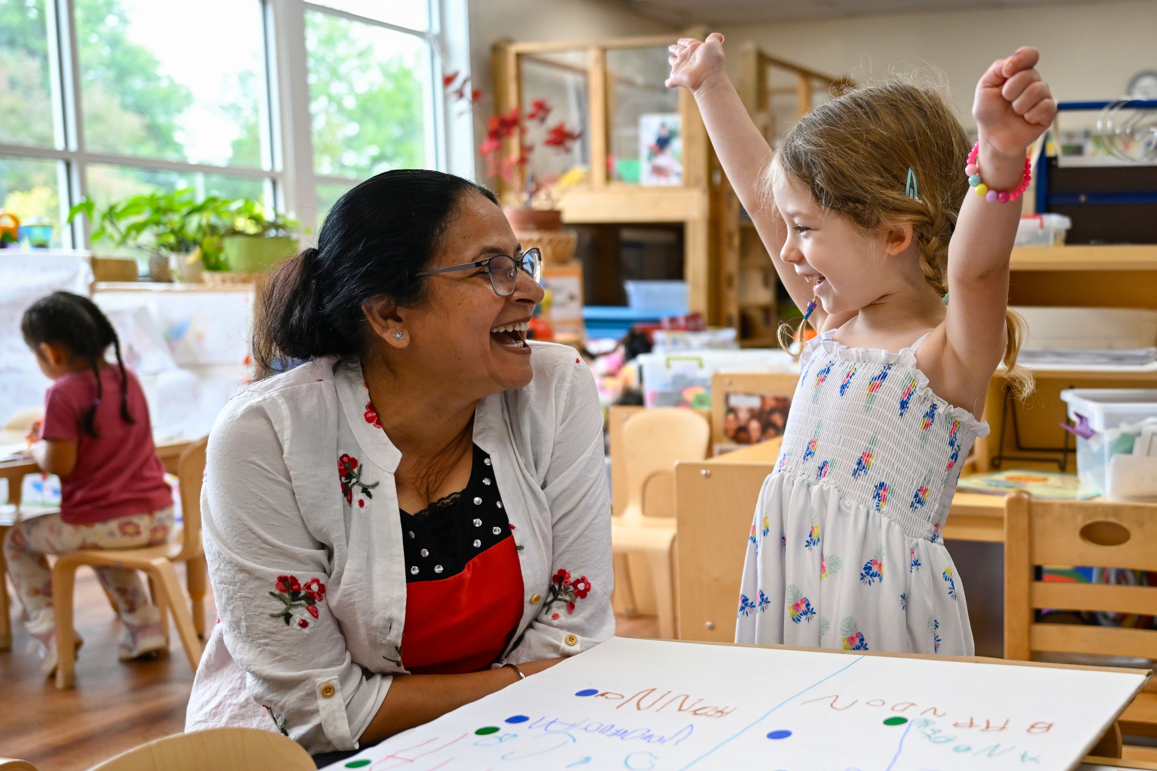 Preschool teacher Jasmeet Kaur, left, watches the reaction of her student Naomi when she discovers that her favorite character of the TV show PAW Patrol won the class vote for the room's favorite character of the show at the ACCA Child Development Center, Thursday, Sept. 19, 2024, in Annandale, Va. The students are getting foundational lessons on how to live in a democracy by allowing them to regularly vote on different things through out the day. (AP Photo/John McDonnell)