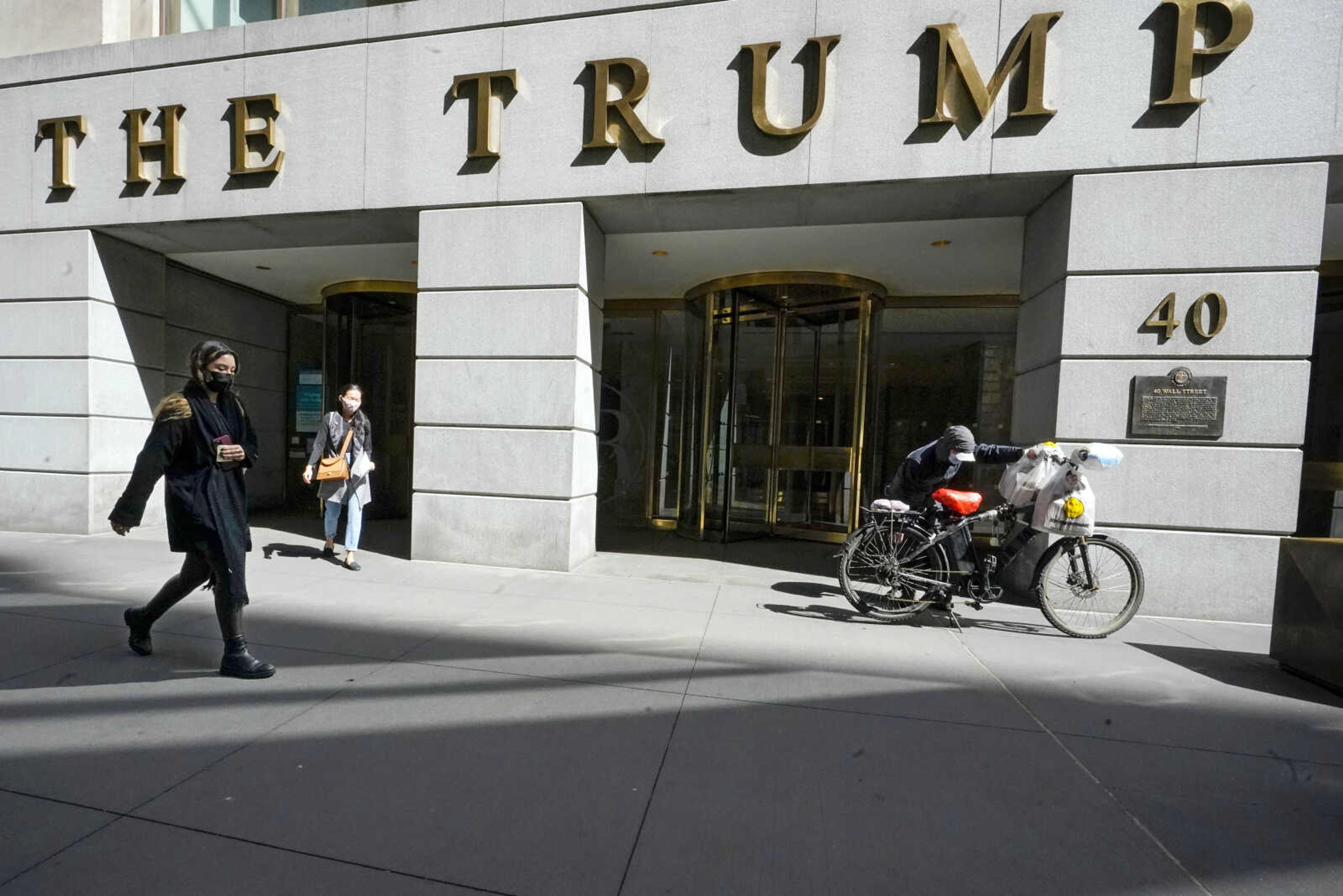 FILE - Pedestrians and a food delivery man are seen outside the Trump building on Wall Street, in New York's Financial District, March 23, 2021. New York Judge Arthur Engoron, ruling in a civil lawsuit brought by New York Attorney General Letitia James, found that Trump and his company deceived banks, insurers and others by massively overvaluing his assets and exaggerating his net worth on paperwork used in making deals and securing loans. (AP Photo/Mary Altaffer, File)