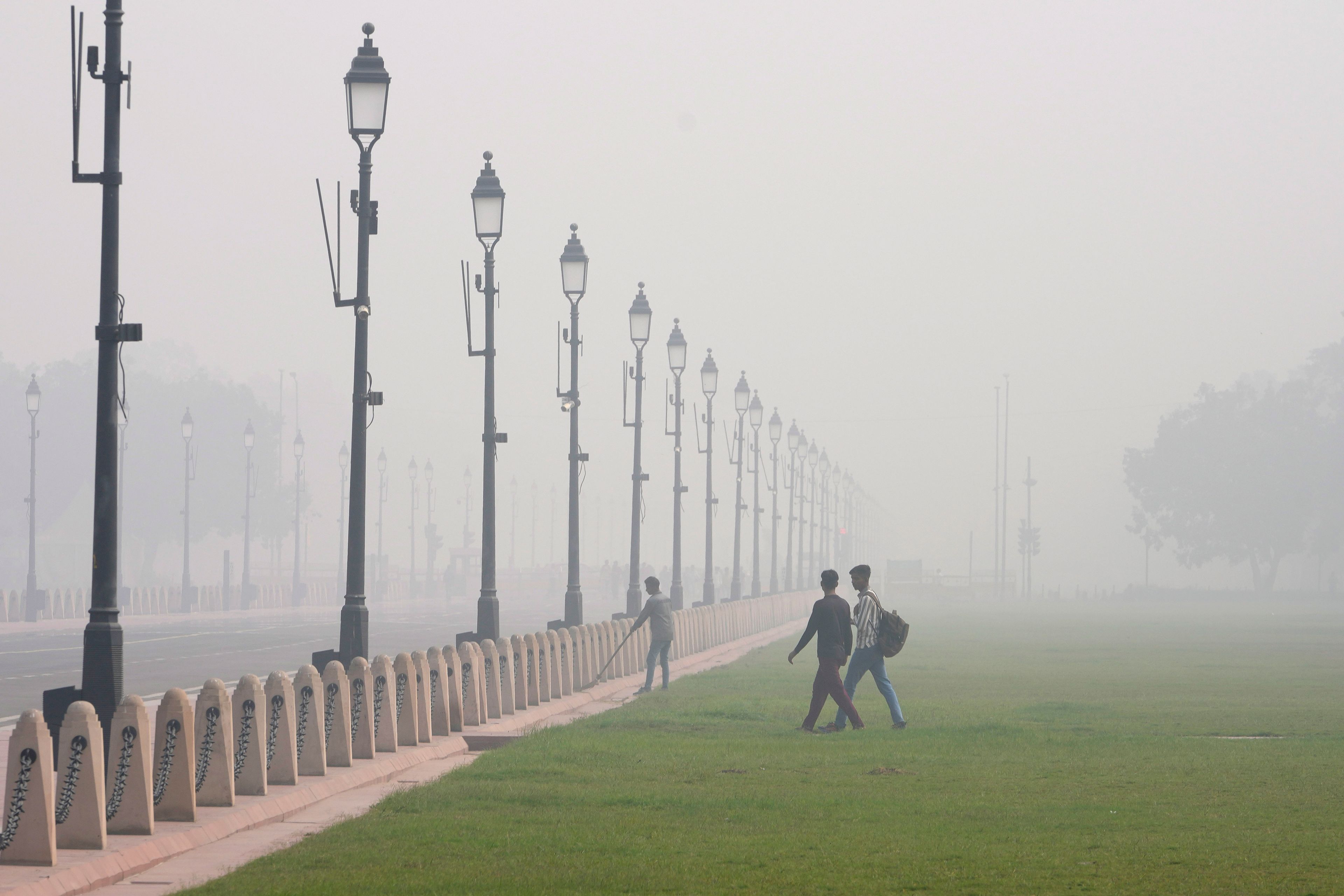 A worker sweeps a pathway surrounded by a thick layer of smog in New Delhi, India, Thursday, Nov. 14, 2024. (AP Photo/Manish Swarup)