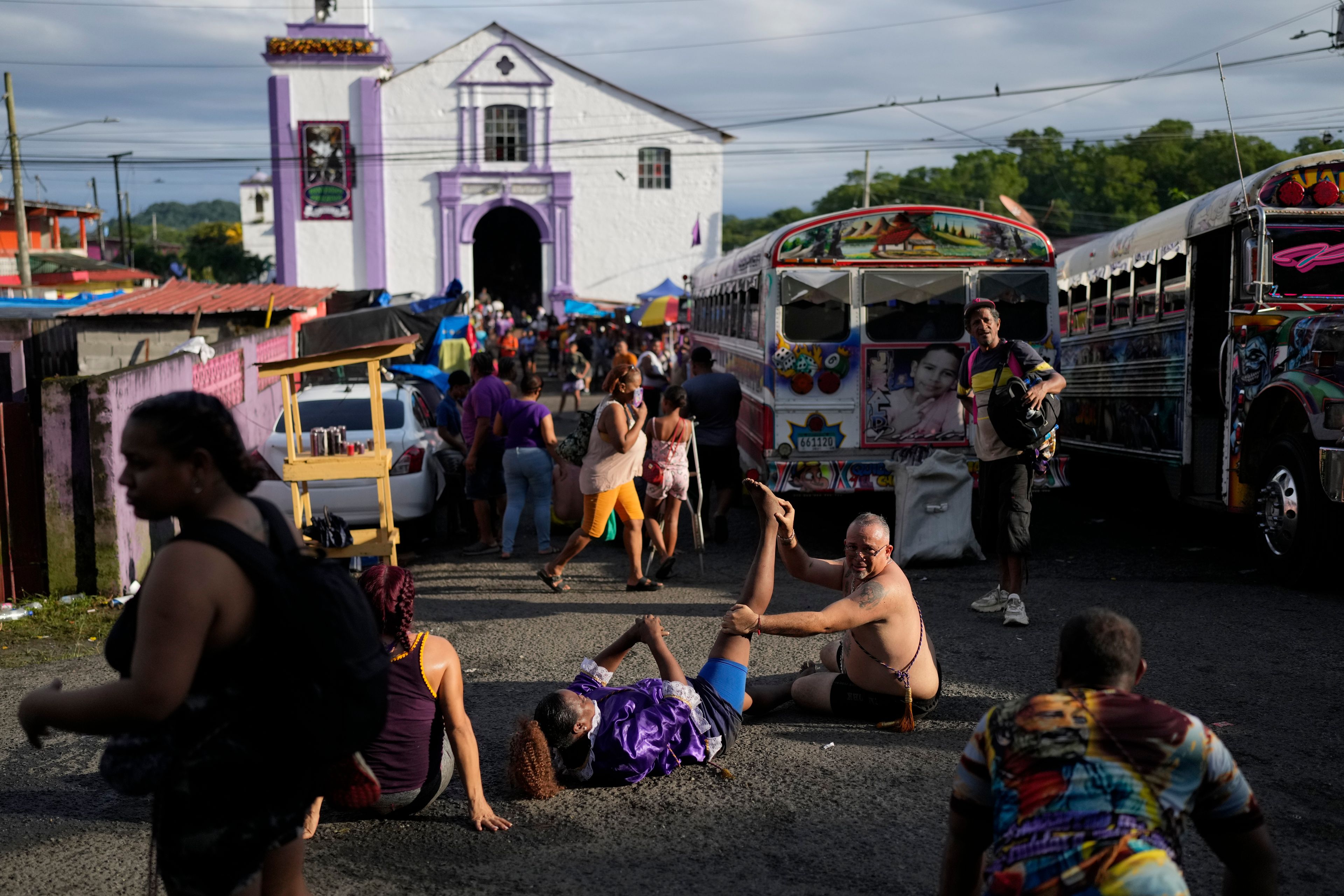 Pilgrim Ernesto Troya stretches his friend's leg as they take a break from crawling on their knees to San Felipe Church, behind, to honor the Black Christ in Portobelo, Panama, Monday, Oct. 21, 2024, during a festival celebrating the iconic statue that was found on the shore in 1658. (AP Photo/Matias Delacroix)