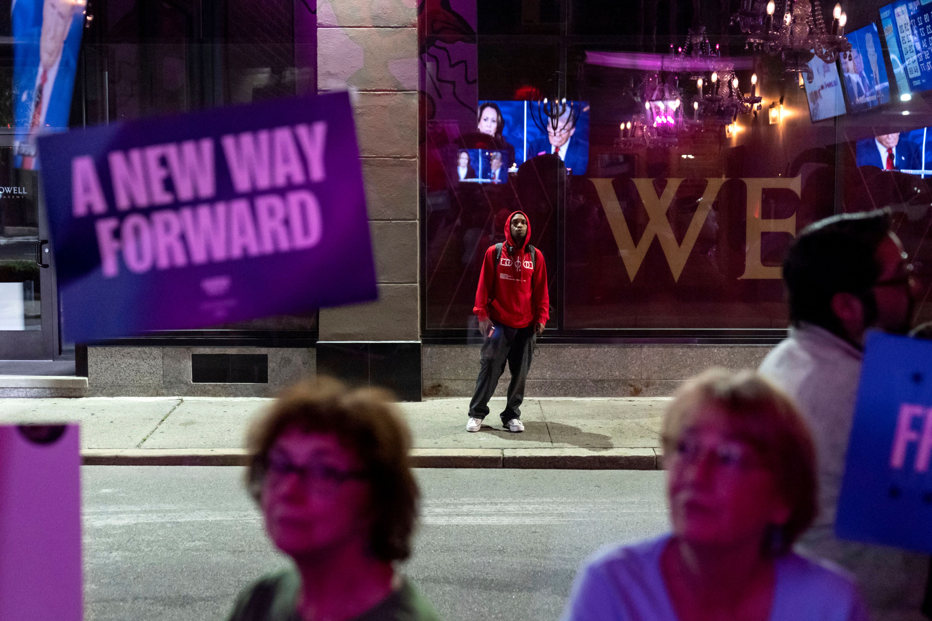 A pedestrian stops to watch a television across the street at Alley Cat showing the presidential debate between Republican presidential nominee former President Donald Trump and Democratic presidential nominee Vice President Kamala Harris, Tuesday, Sept. 10, 2024, in Providence, R.I. (AP Photo/David Goldman)