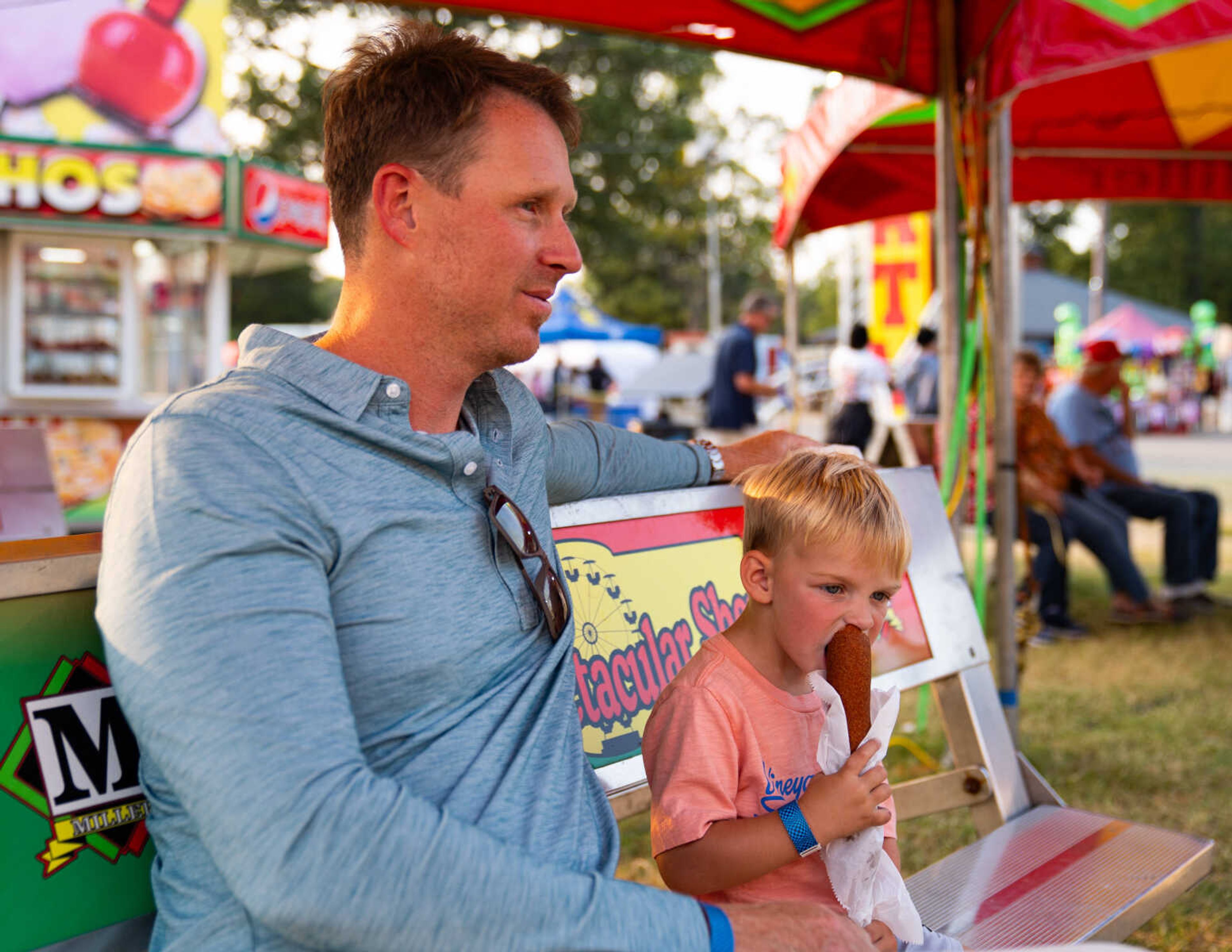 Josh Irby sits by his son, River, as he enjoys a fair staple — a corn dog.