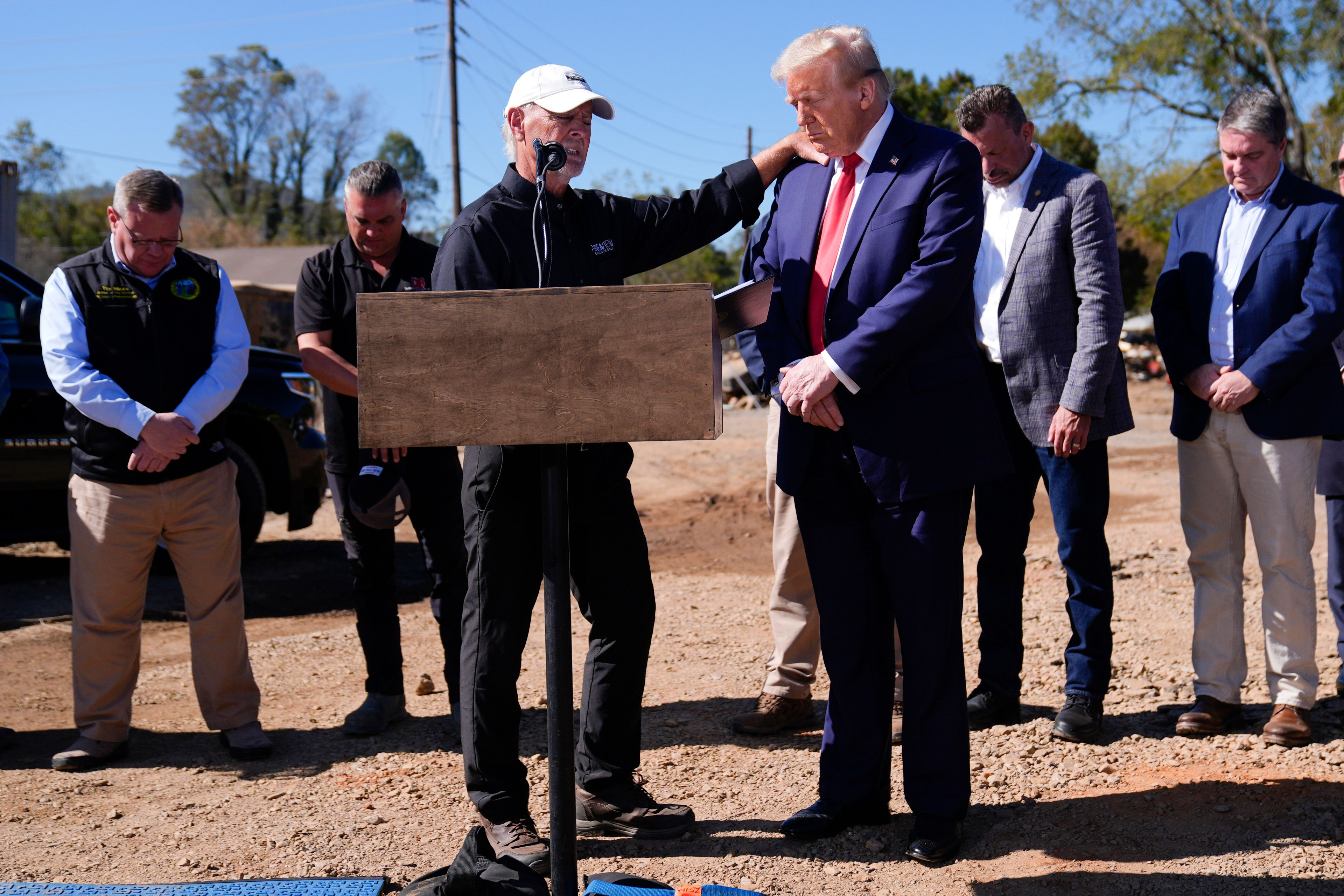 Republican presidential nominee former President Donald Trump prays with Mike Stewart, owner of Pine View Buildings, and others, after delivering remarks on the damage and federal response to Hurricane Helene, Monday, Oct. 21, 2024, in Swannanoa, N.C. (AP Photo/Evan Vucci)